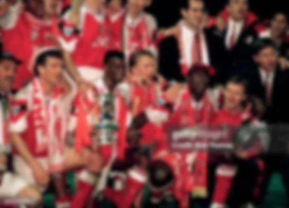 Blurred image of a sports team celebrating victory, wearing red and white uniforms with a trophy.