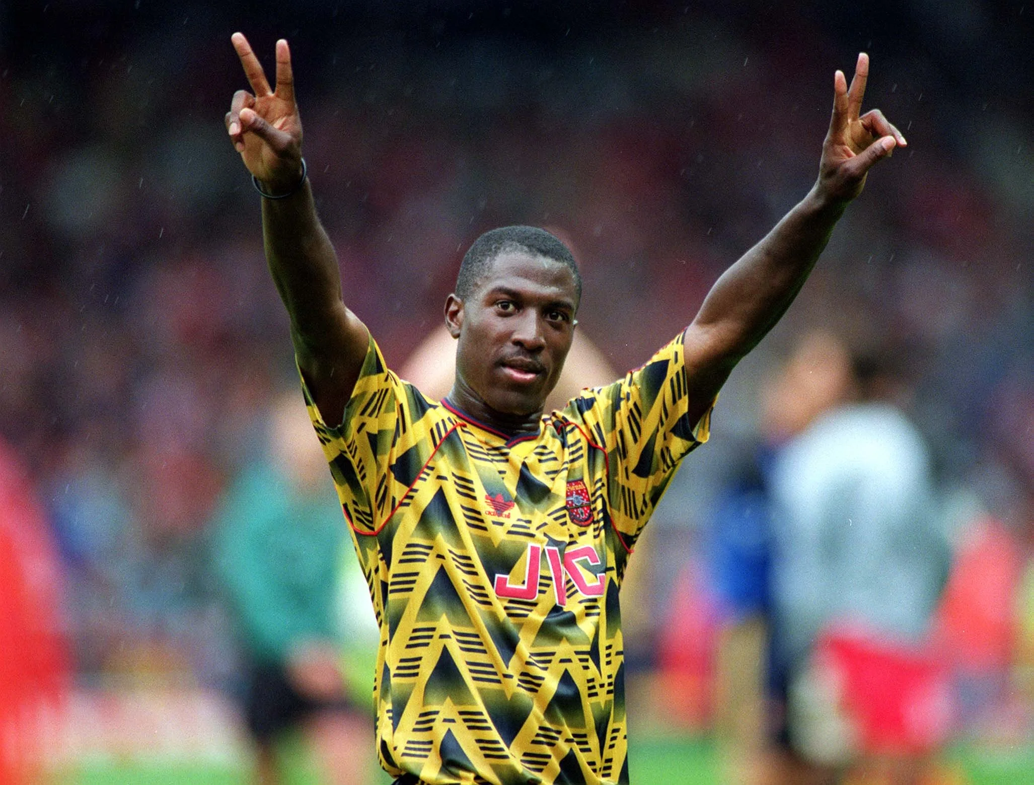 Kevin Campbell is wearing the Arsenal bruised banana away kit, holding up two fingers on each hand.