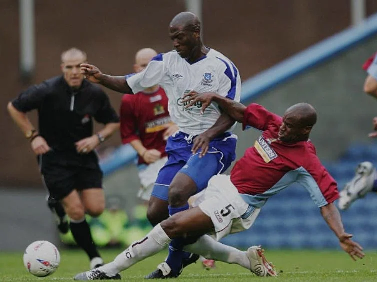 Football match action with Kevin Cmpbell in a white and blue kit, with a referee in the background.