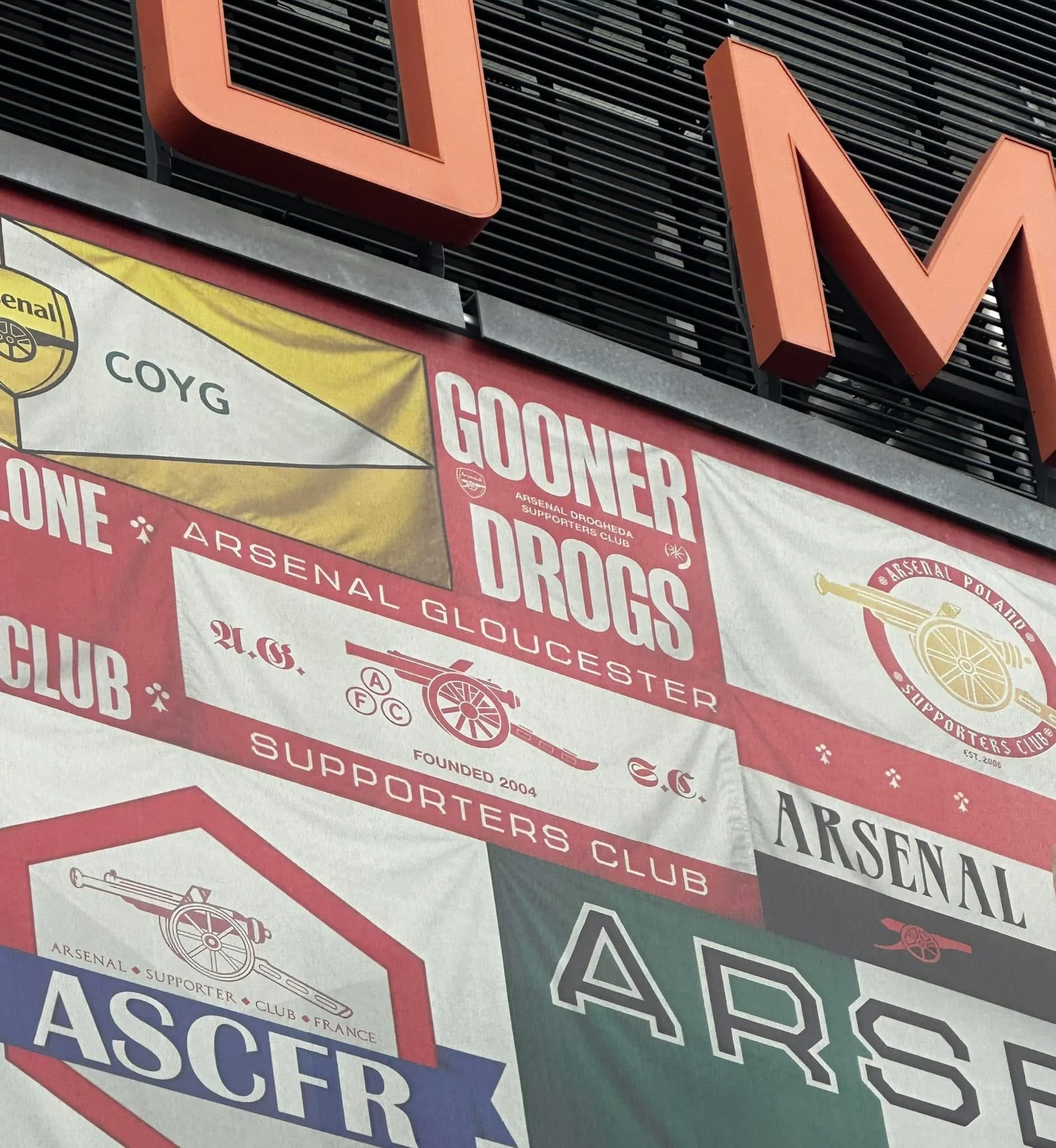 Banners of Arsenal supporters clubs from various regions are displayed, featuring club names and logos, including "Gooner Droghe," "Arsenal Gloucester," and "Arsenal Poland."