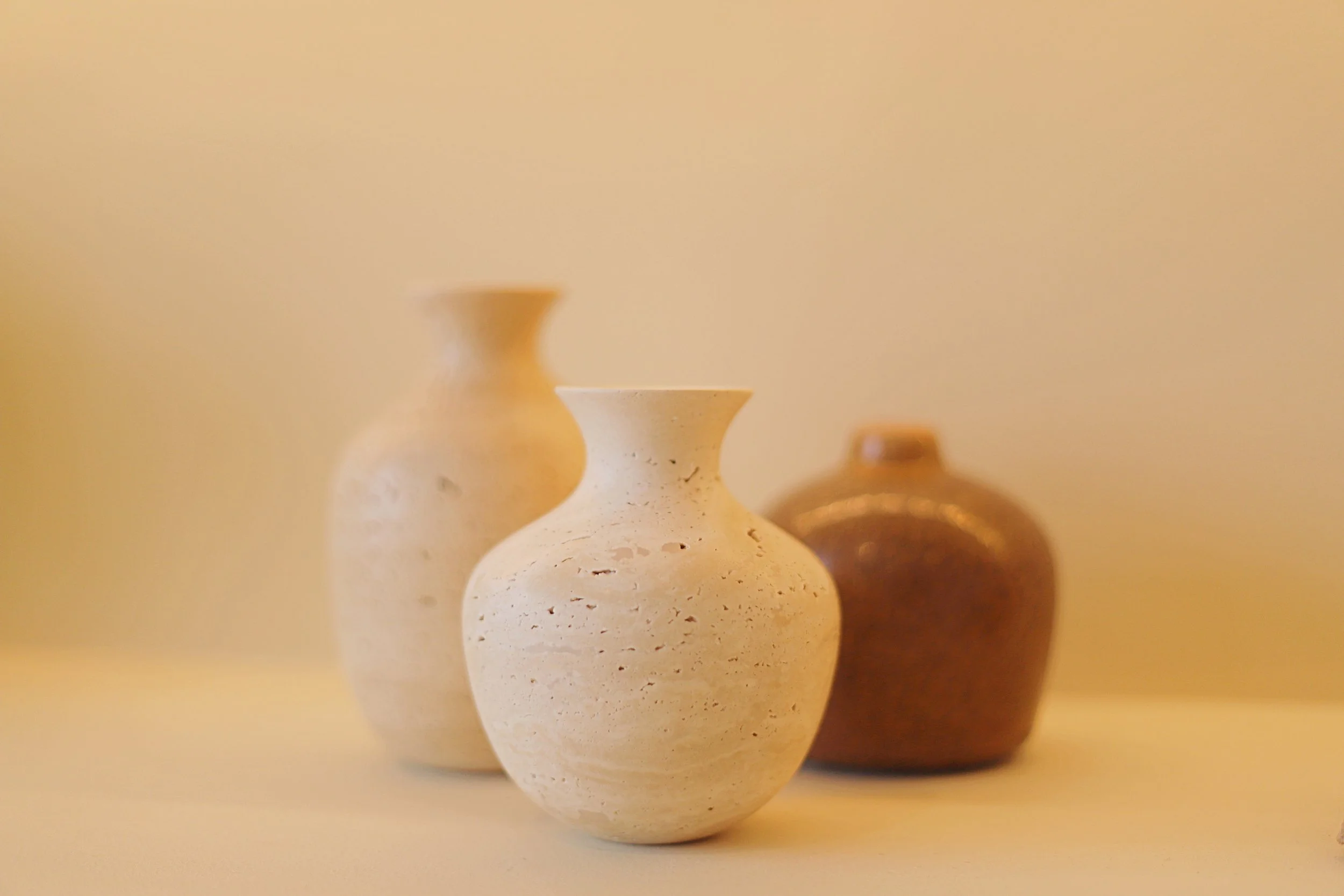 Three small ceramic vases of different colors and textures on a beige surface against a beige background.