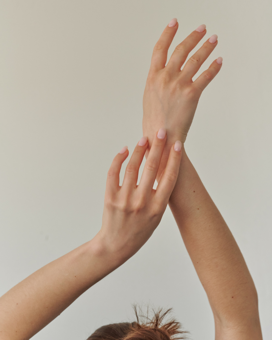 Two hands gently touching each other against a plain background.