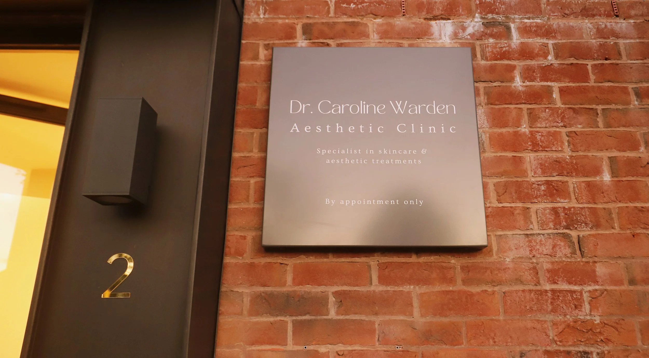 Classy external Sign for Dr. Caroline Warden Aesthetic Clinic in Hale Cheshire on a brick wall, indicating it is a skincare and aesthetic treatments clinic by appointment only.