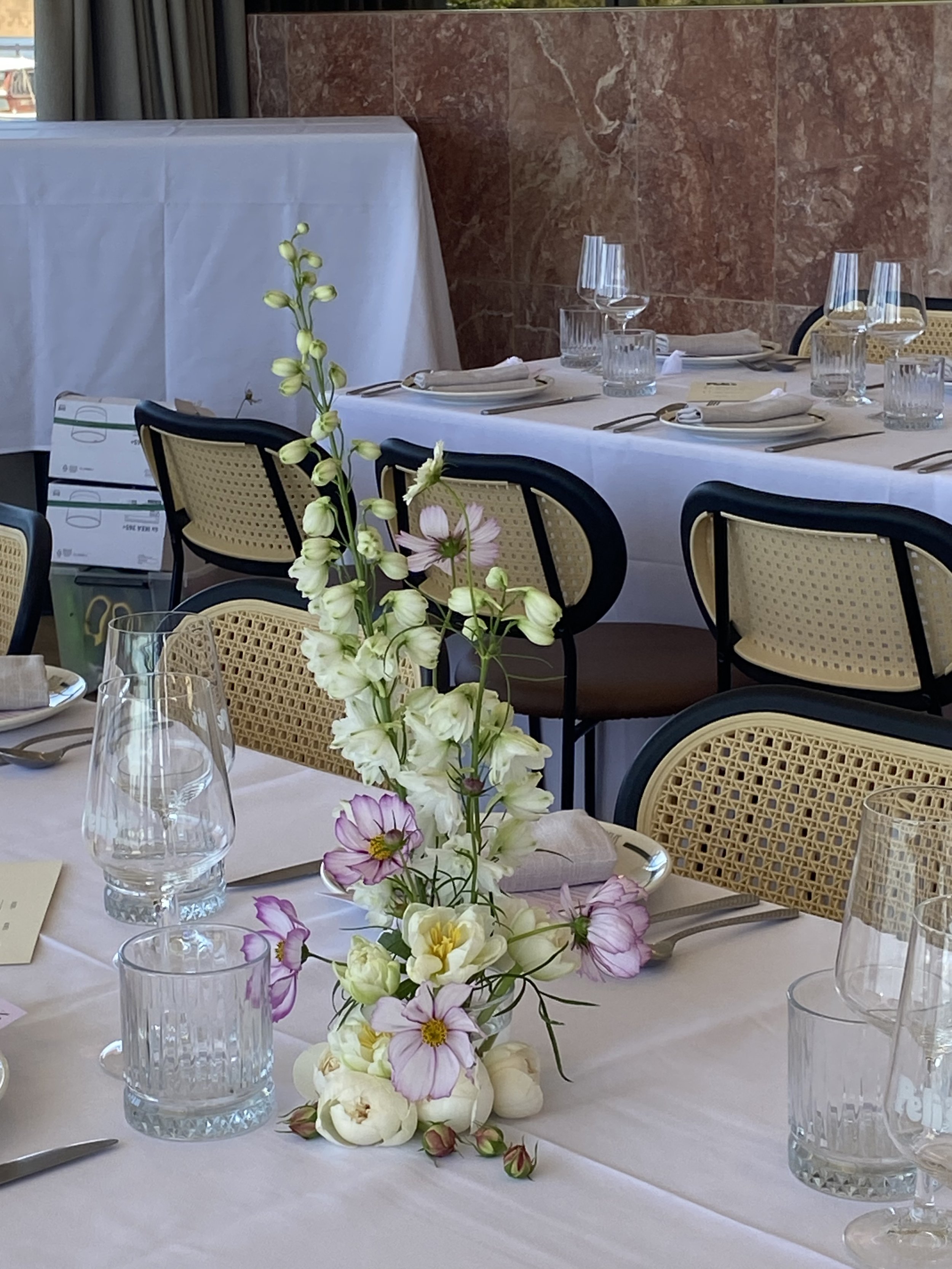 Elegant dining table set with floral centerpiece, wine glasses, water glasses, and place settings, in a well-lit room with a brick accent wall.
