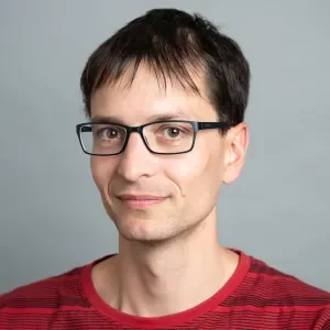 A man with no beard, with dark short hair, wearing a red T-shirt