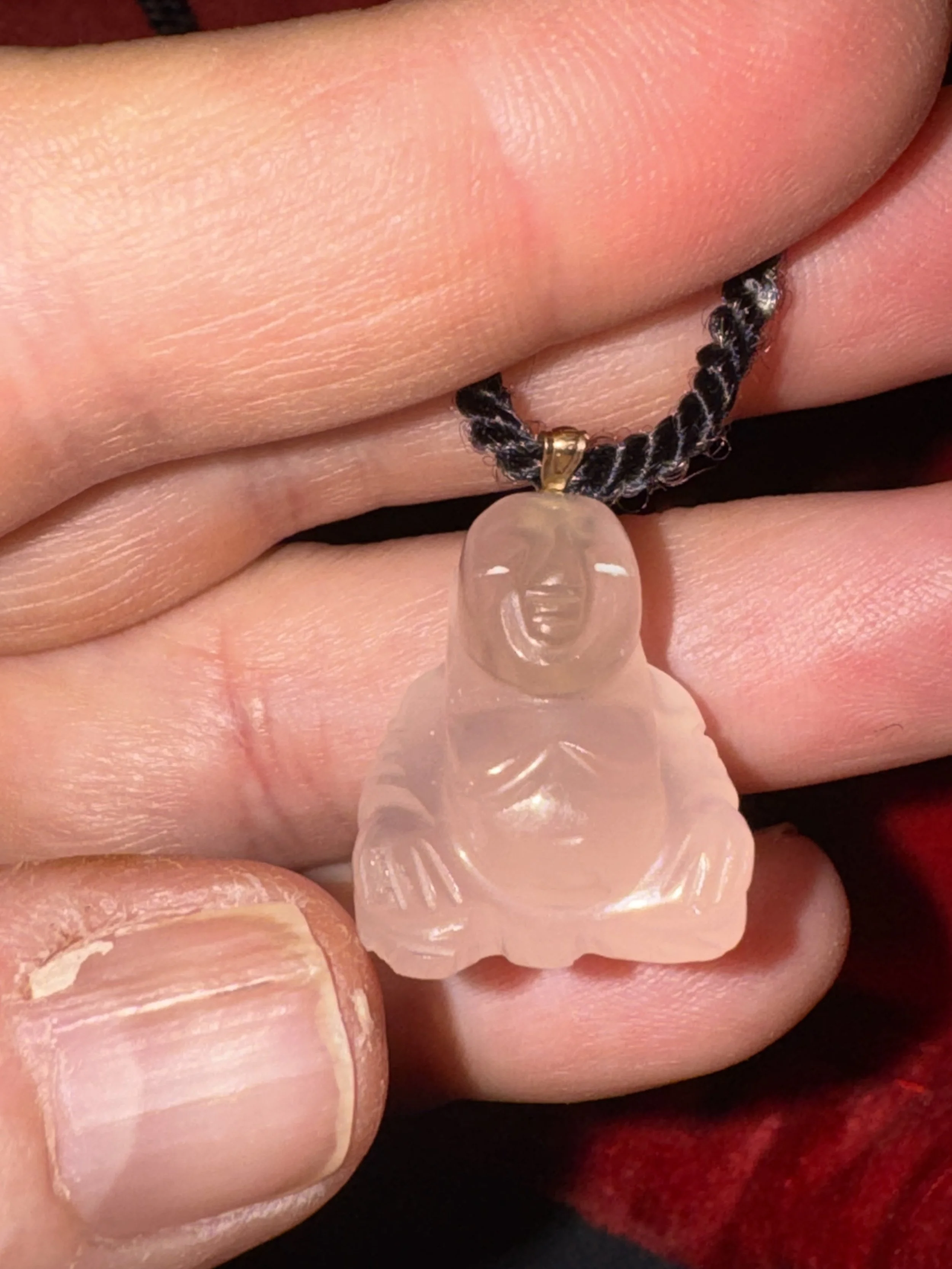 A person holding a pendant necklace featuring a carved pinkish-white Buddha figure on a dark, braided cord.