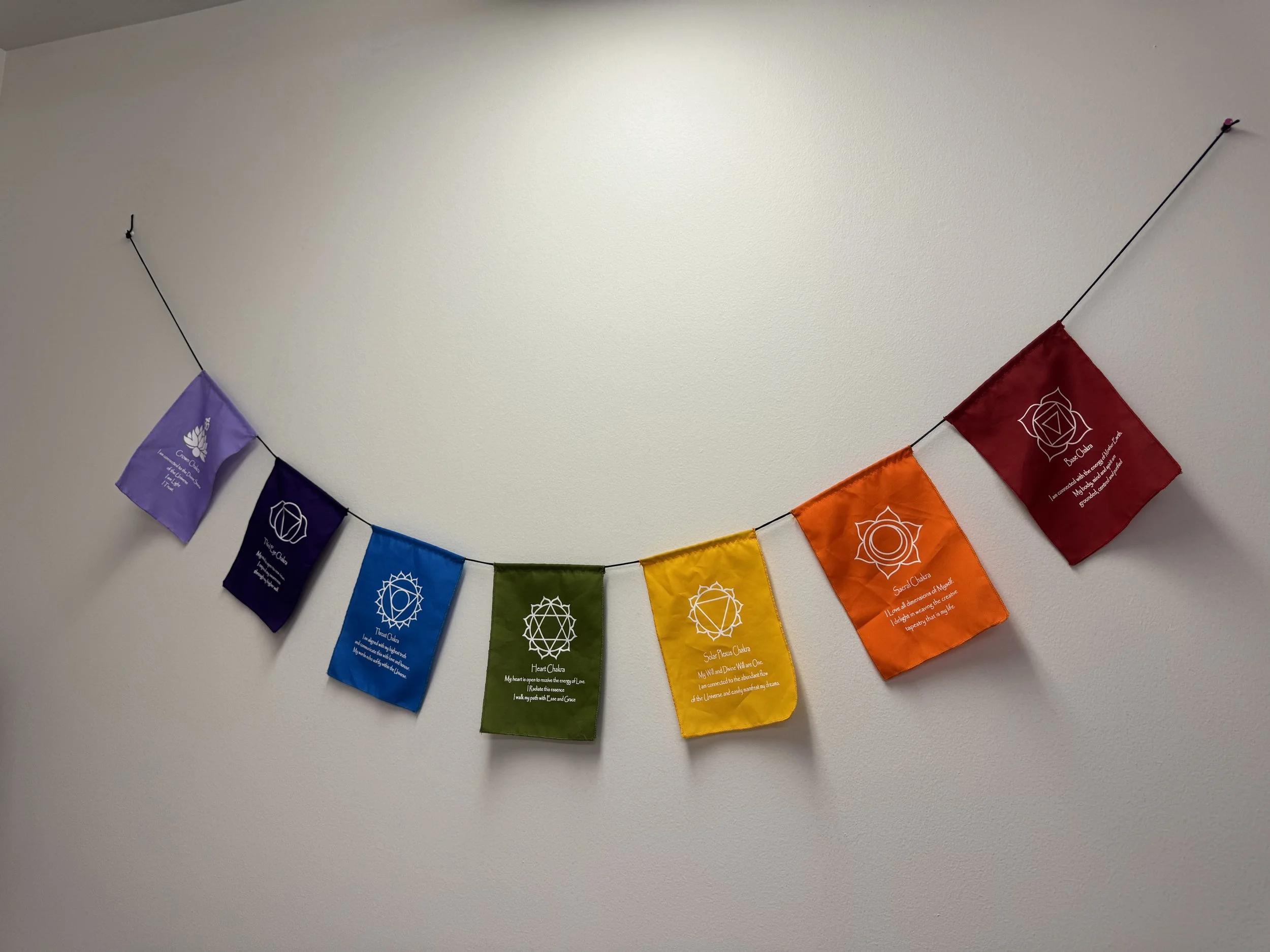 A rainbow-colored string of cloth prayer flags hanging on a wall, each flag featuring different symbols and text.