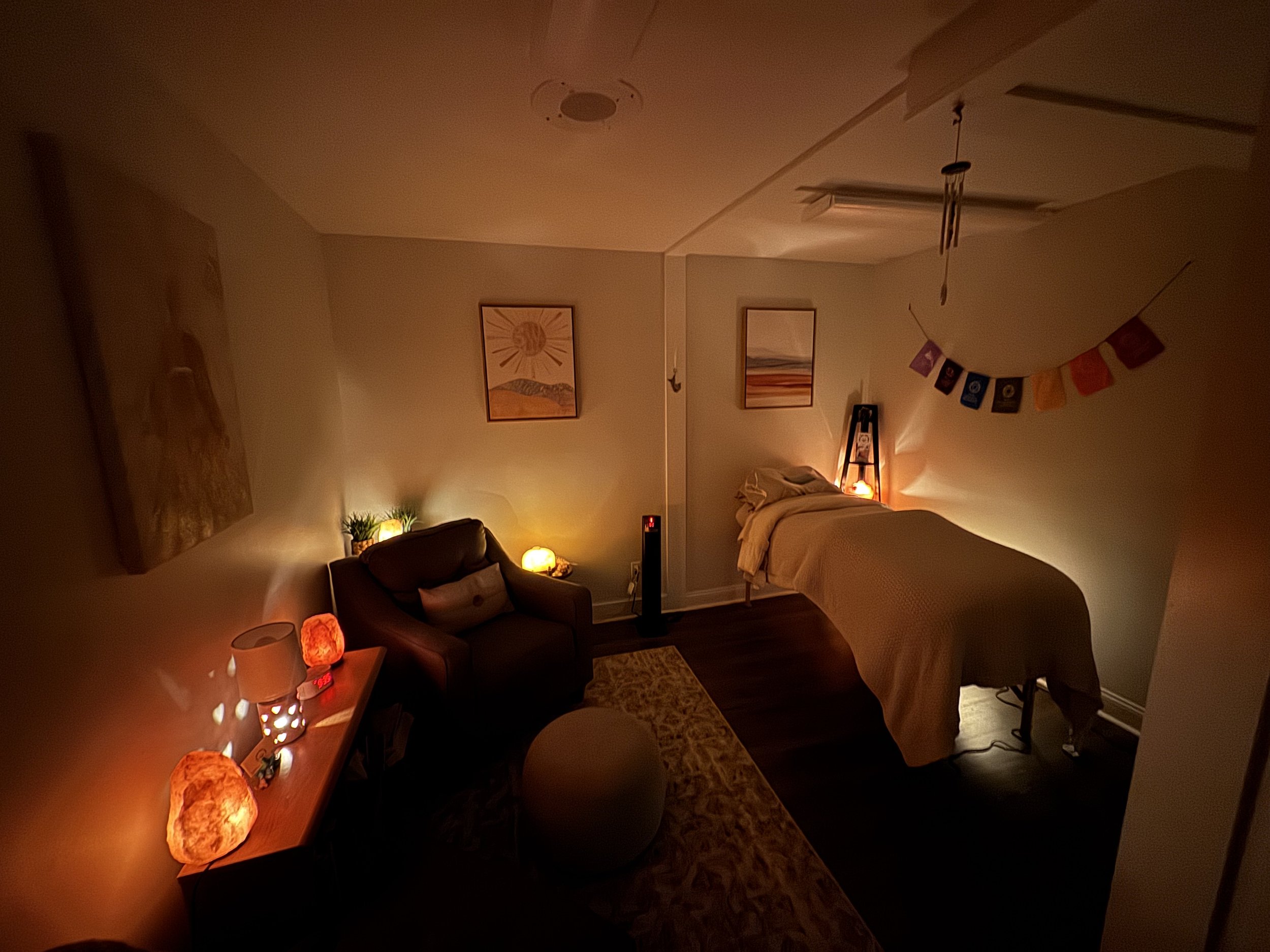 Cozy, dimly lit room with a massage table, decorated with Himalayan salt lamps, warm lighting, and a comfortable chair.