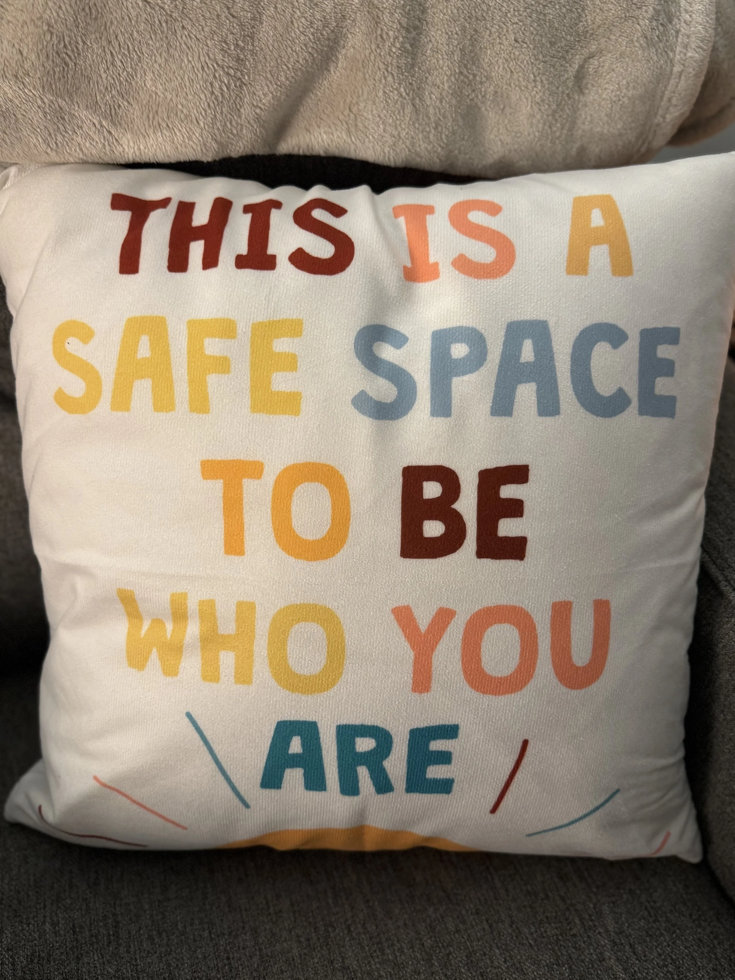 Decorative pillow with the of message: "This is a safe space to be who you are" in colorful letters.
