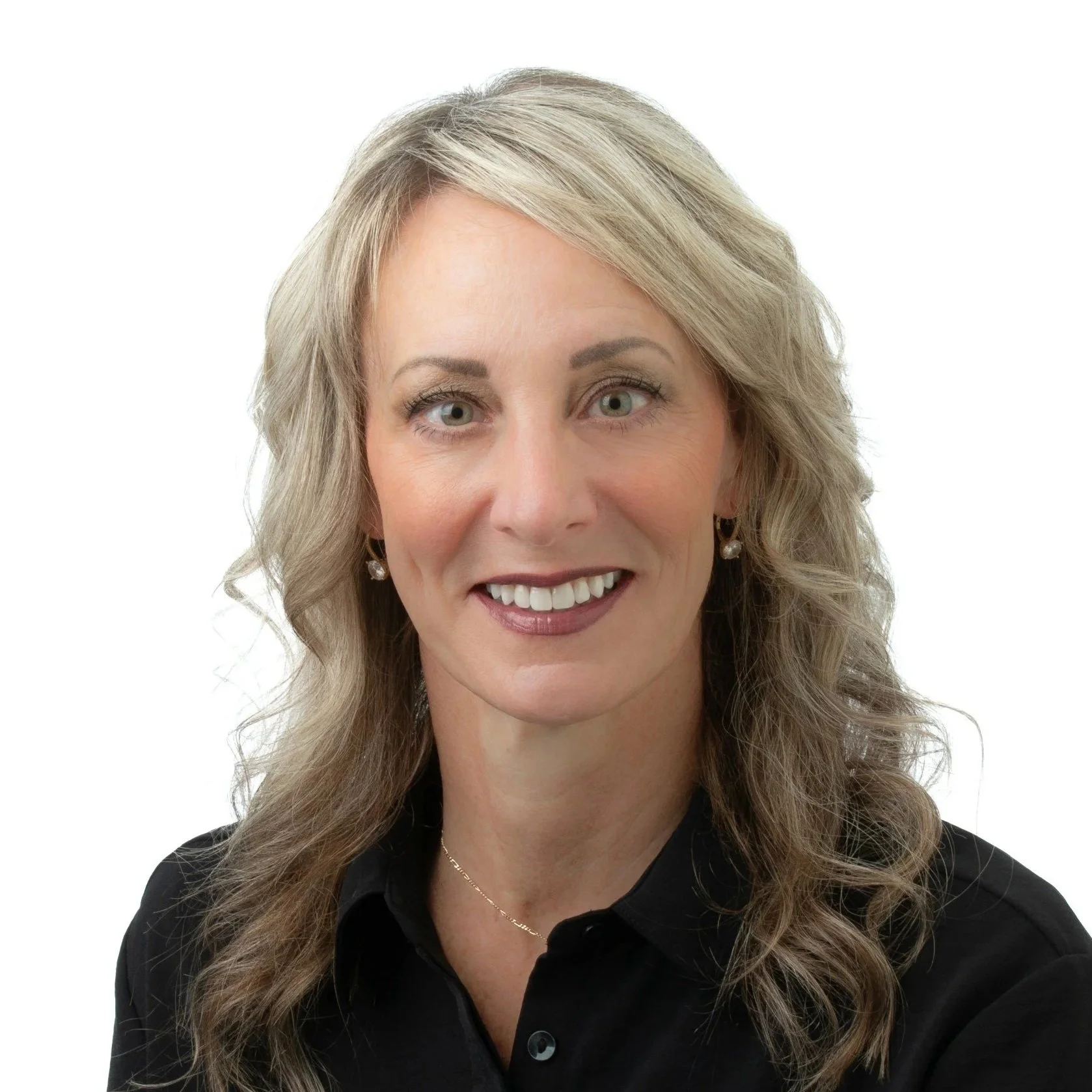 A portrait of a smiling woman with gray hair, wearing a pink blazer, a multicolored scarf, and dangling earrings, against a white background.