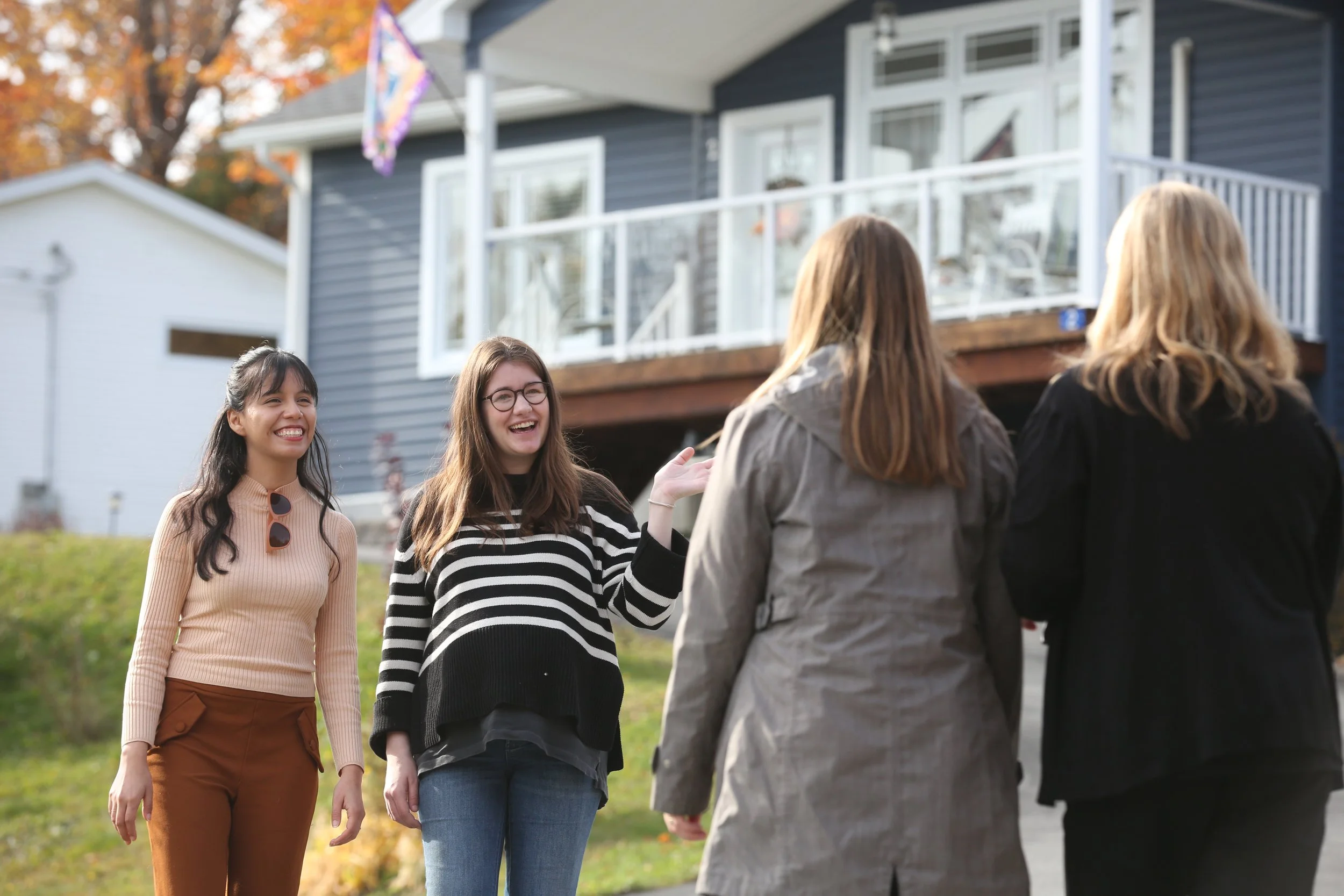 Four women talk and laugh outside in front of a house during fall