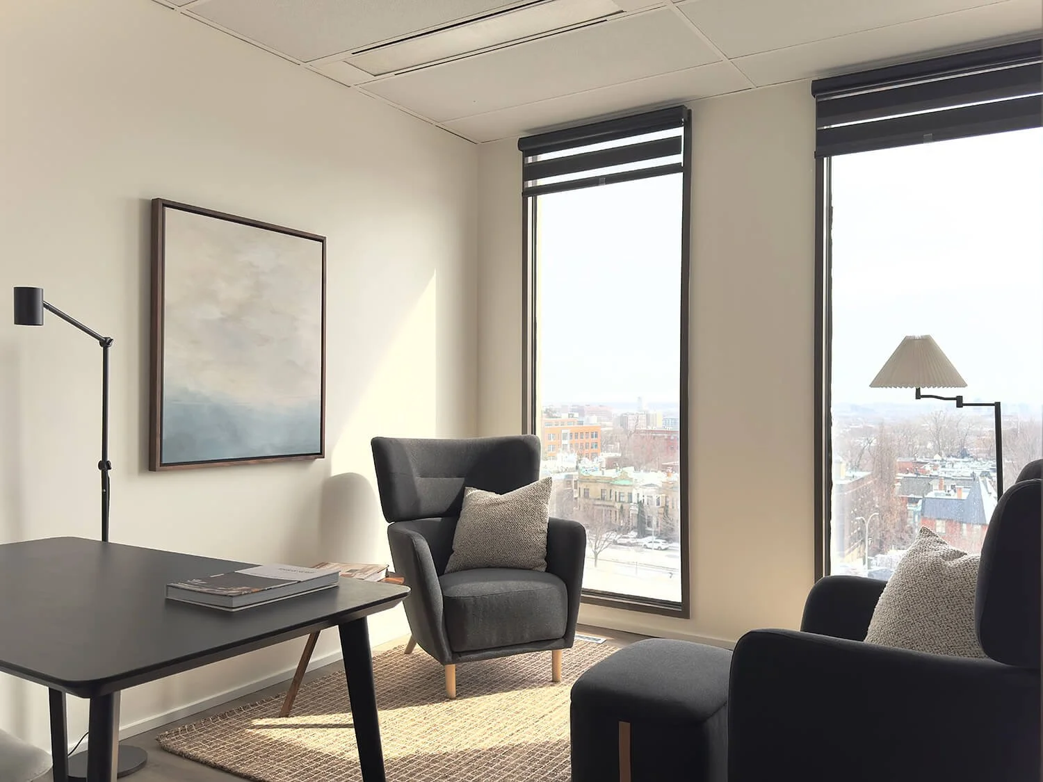 Salon avec fauteuils, tapis, tableau sur le mur, lampes, grande fenêtre avec vue sur la ville