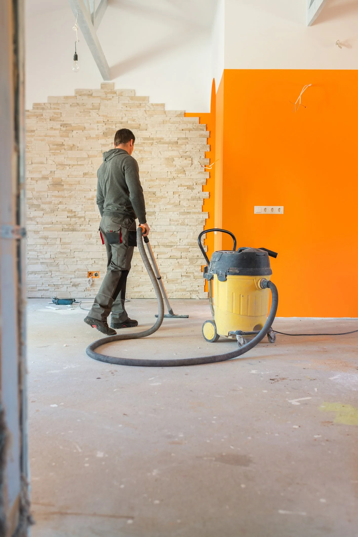 Man werkt aan muur met oranje en witte verf, stofzuiger en bouwtools