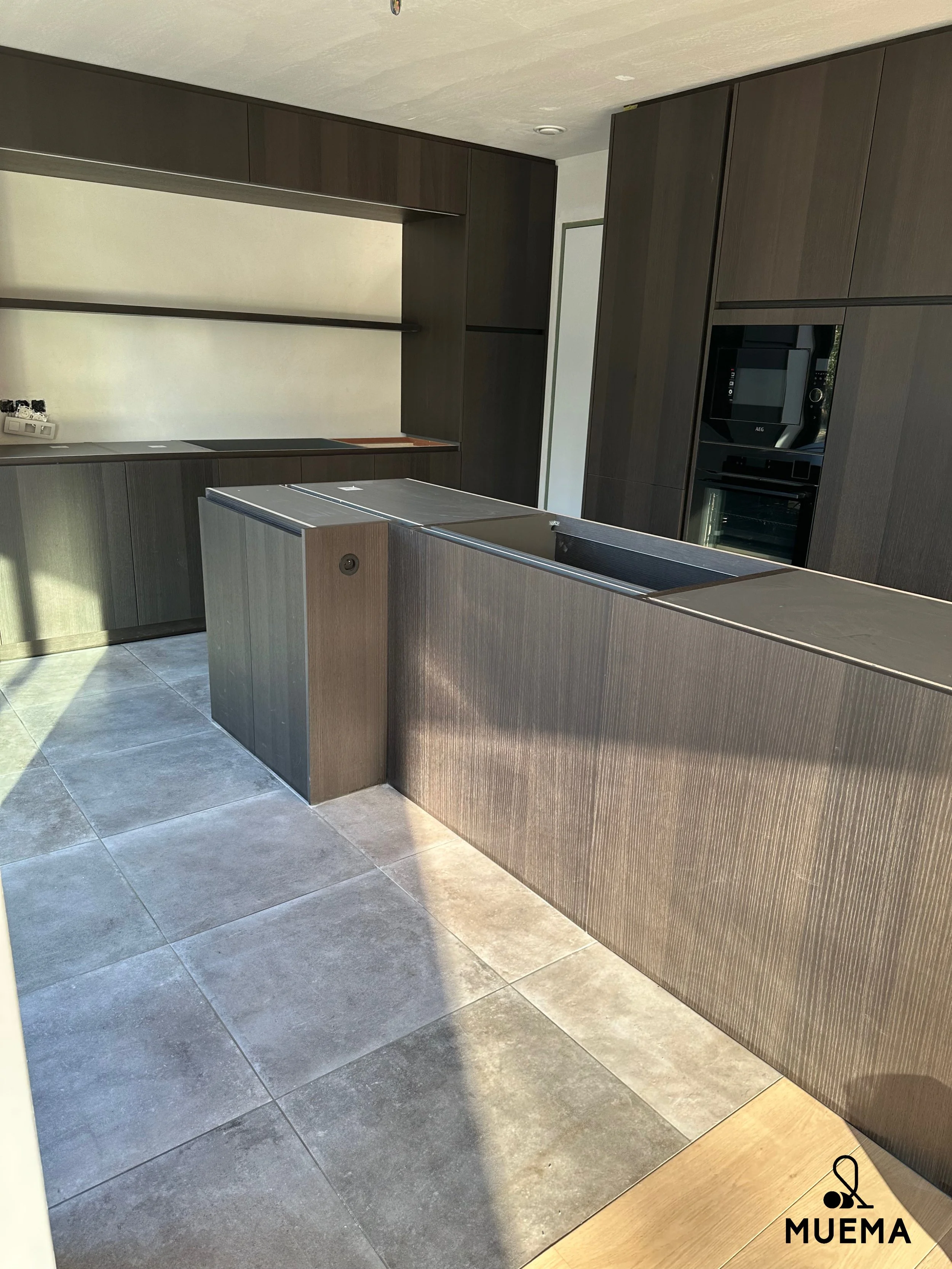 Moderne keuken met donkerhouten kasten, een eiland en ingebouwde oven, op een vloer met grote grijze tegels.