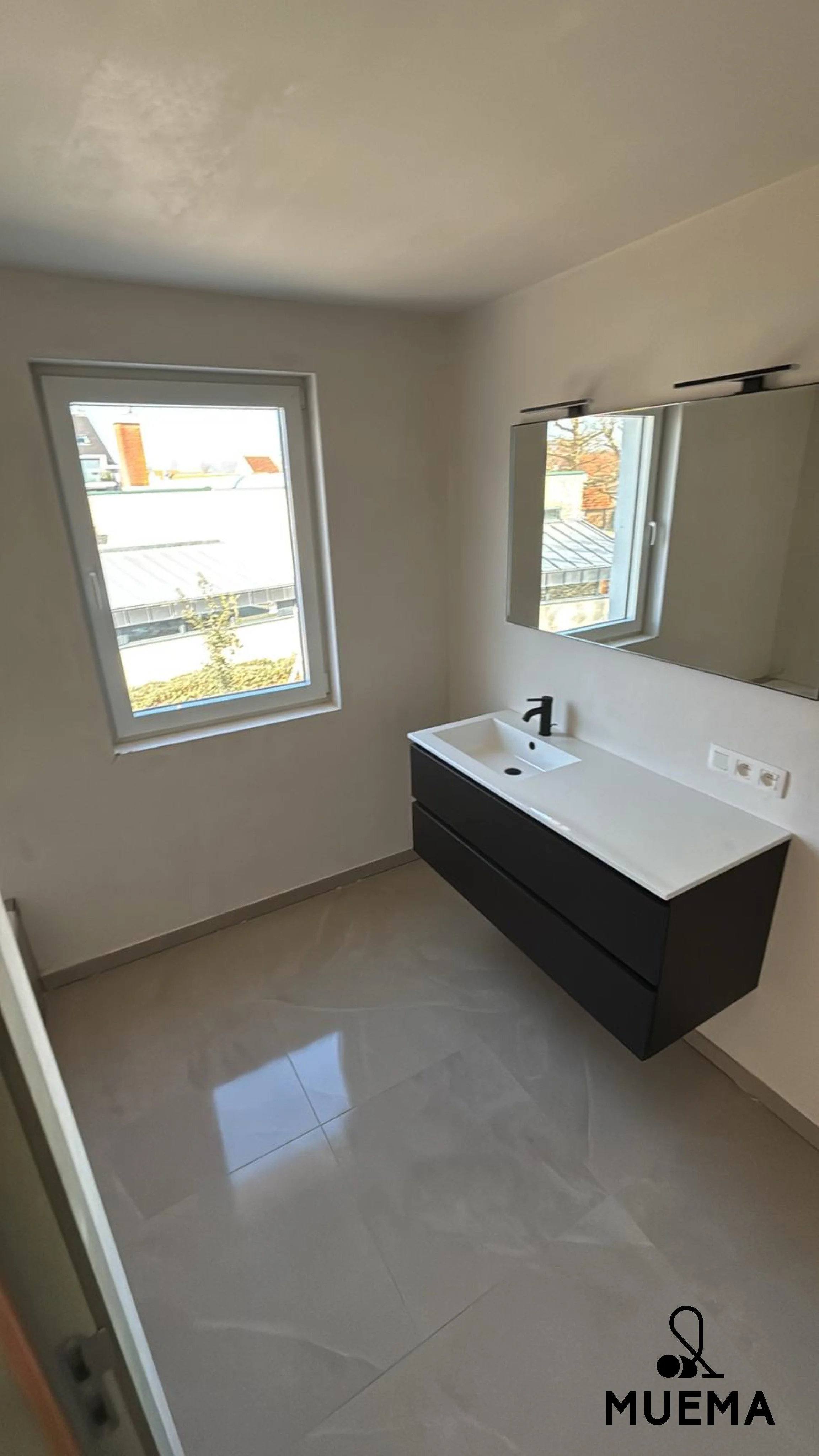 Een lege badkamer met een wastafel, spiegel en twee ramen, met een tegelvloer.