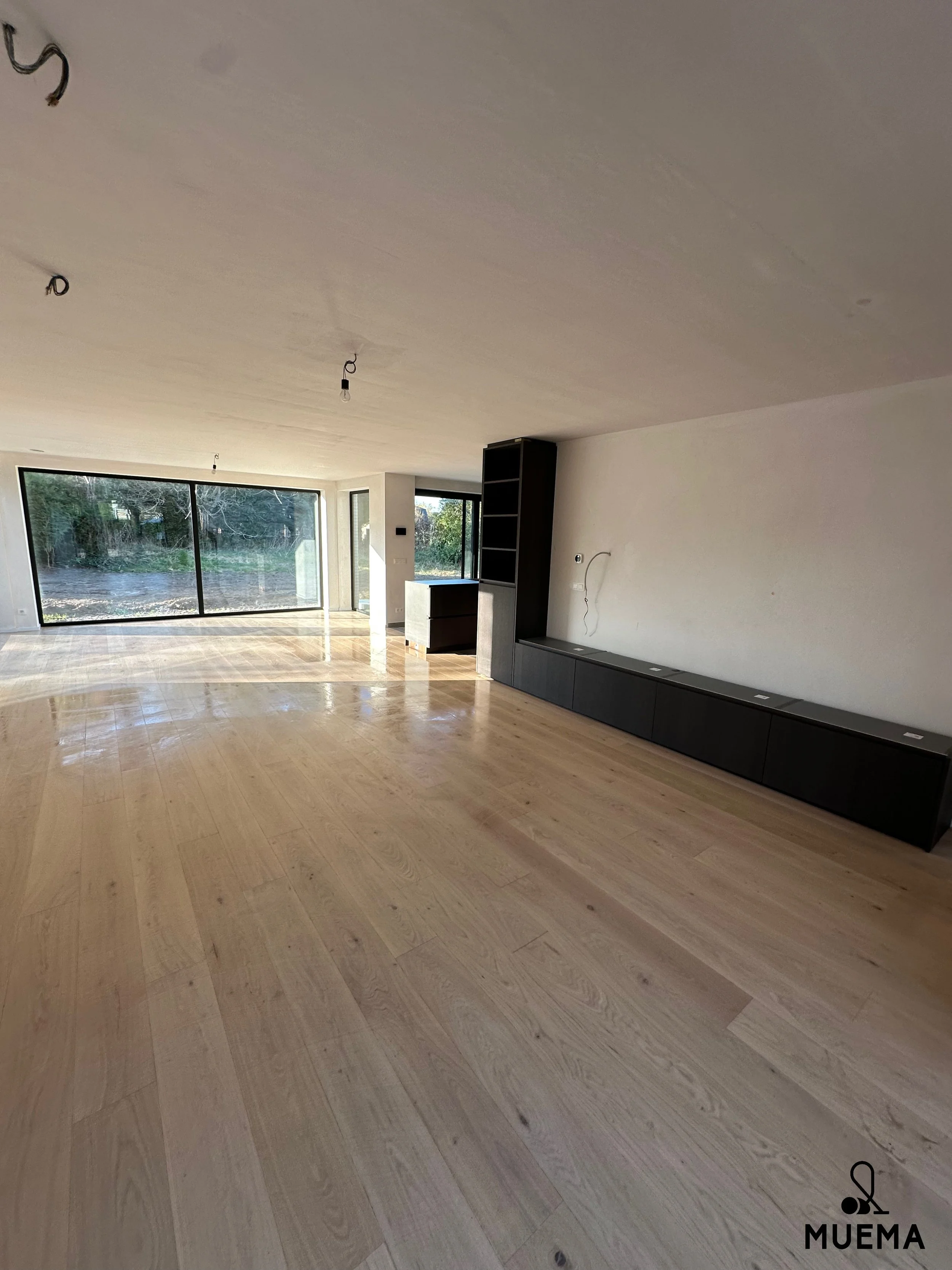 Onbezetten, leeg woonhuis met grote glazen schuifdeuren, houten vloer, witte muren en een ingebouwde koffiekast.