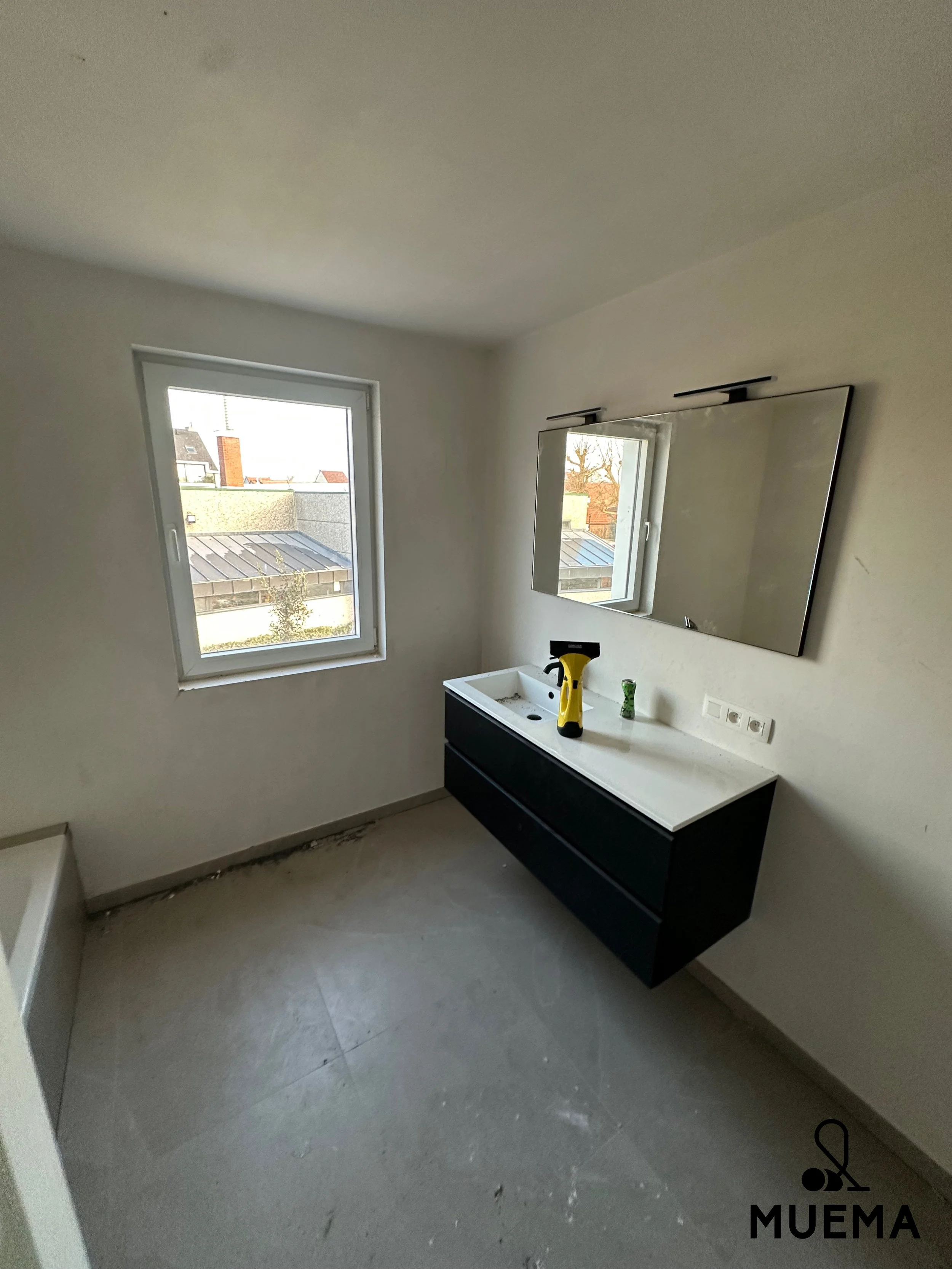 Onbehandelde badkamer met wit wastafelmeubel, spiegel, twee ramen, en een natuurstenen vloer.