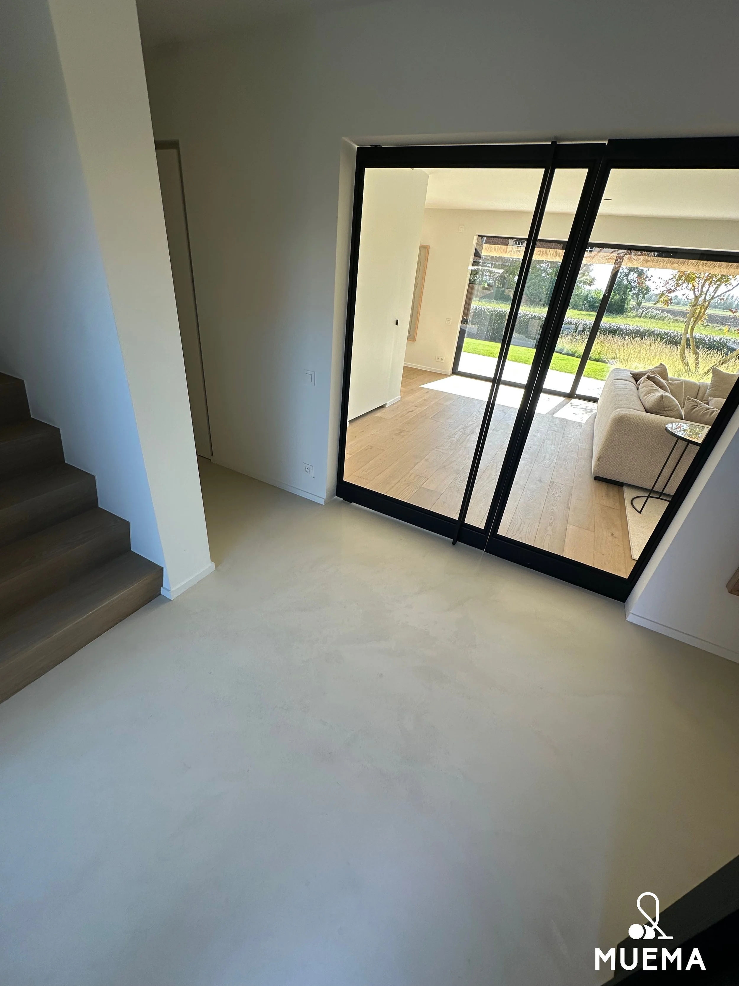 Leeg wit kamer met houtenvloer en grote glazen schuifdeuren die uitkijken op een tuin.