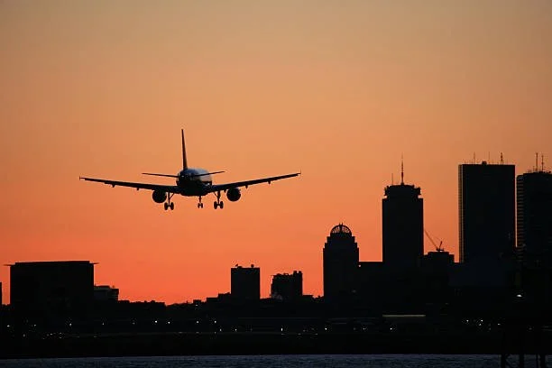 An airplane flying over a city skyline during sunset.