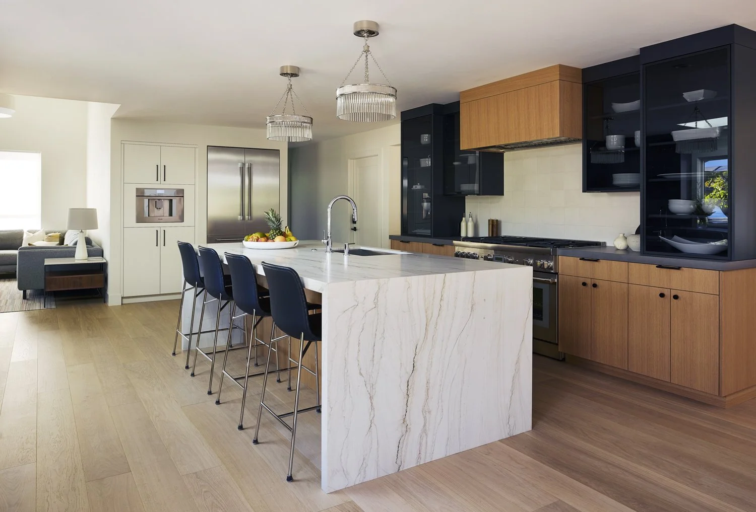 Modern kitchen with white marble island, black and wood cabinets, stainless steel refrigerator, and pendant lights.