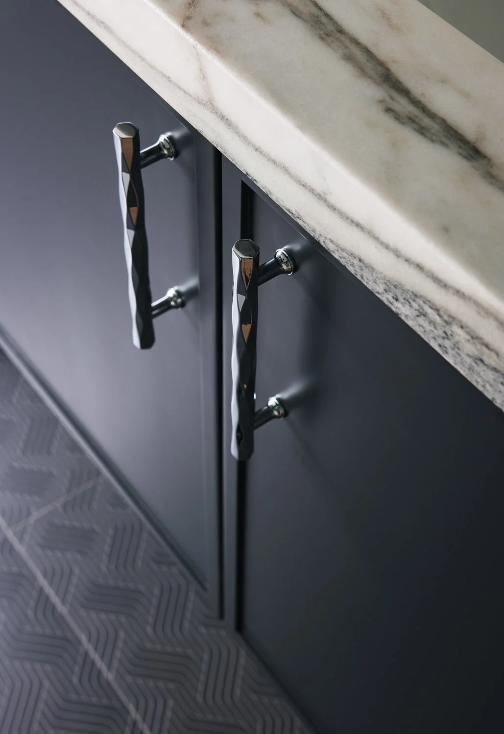Close-up of black kitchen cabinet doors with two modern, twisted silver handles beneath a white marble countertop.