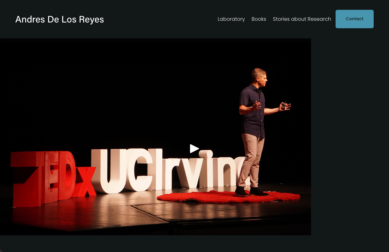 A man giving a presentation on stage with large red and white TEDxUCIrvine letters behind him, standing on a small red rug.