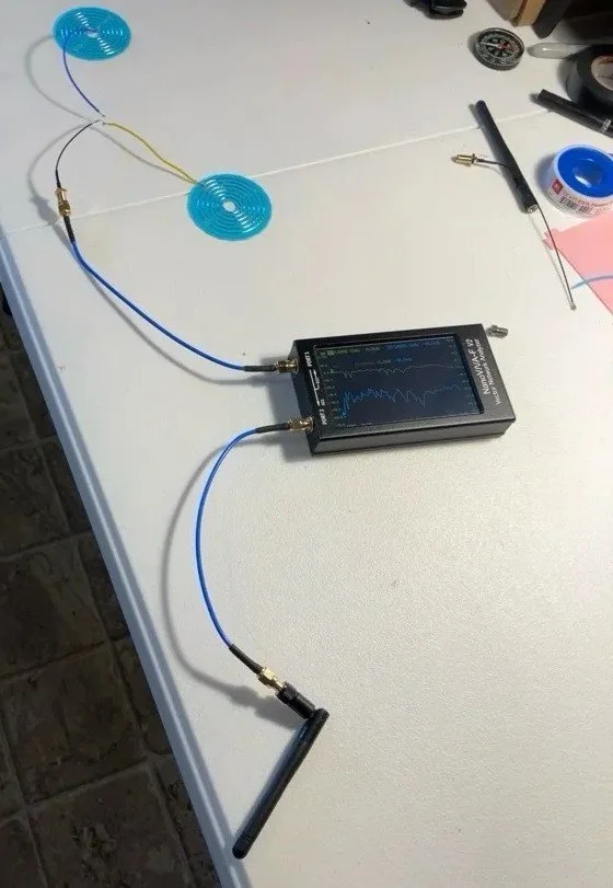 A handheld oscilloscope on a white table with wires connected to blue and yellow circular electrodes, likely conducting a physics or electronics experiment.