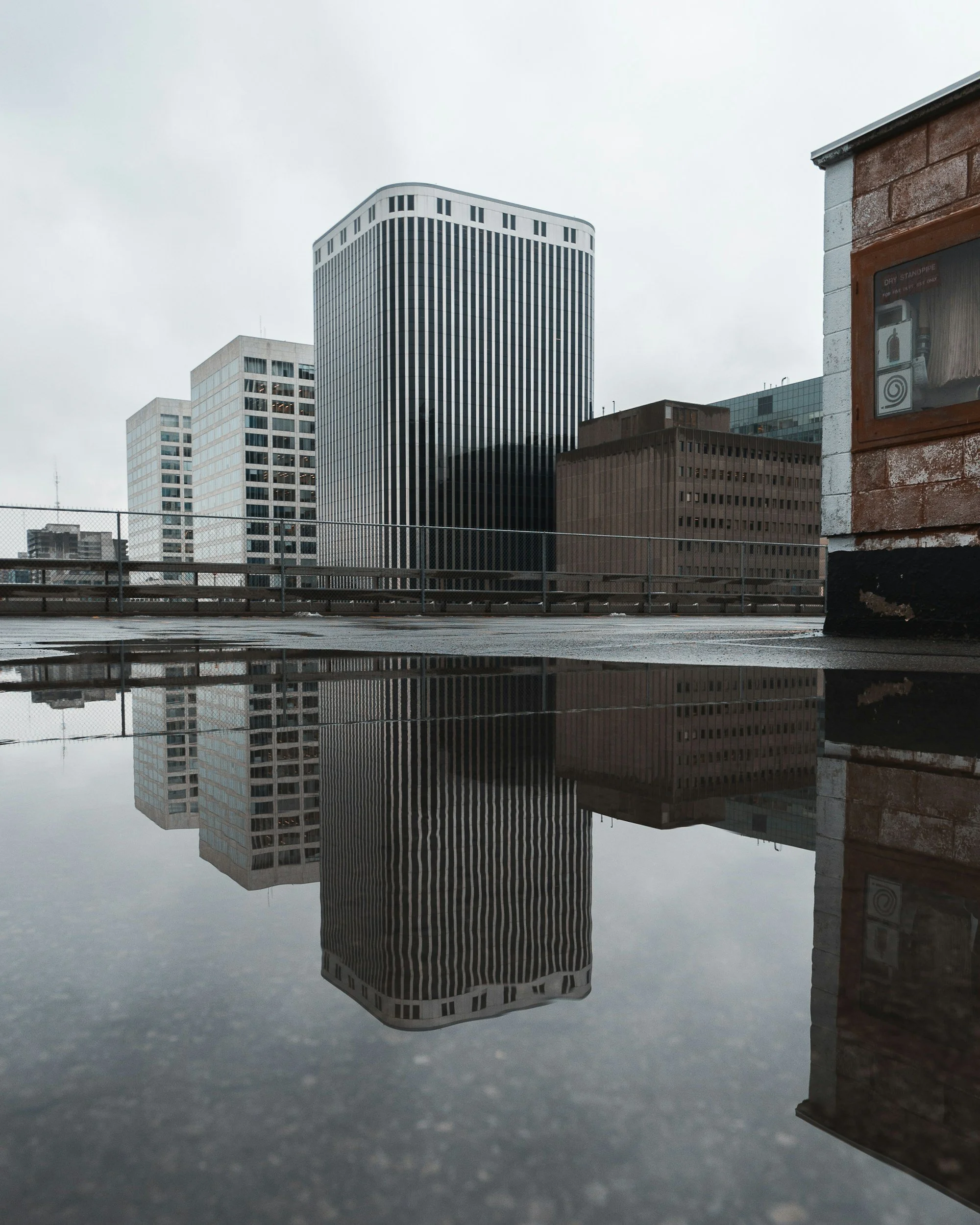 Reflection of tall modern office buildings on a wet rooftop surface on a cloudy day.