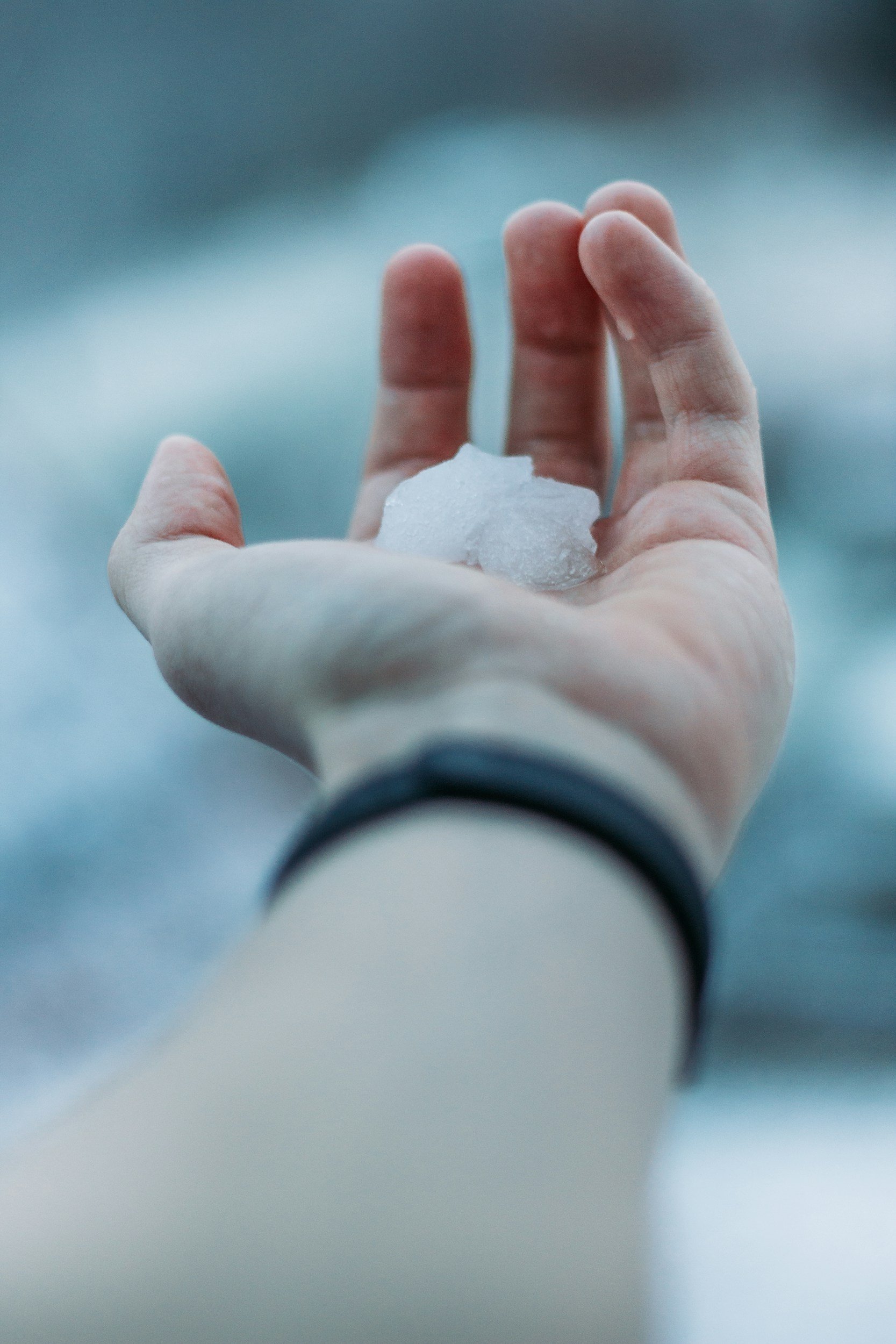 A person holding a piece of ice in their hand over an outdoor background.
