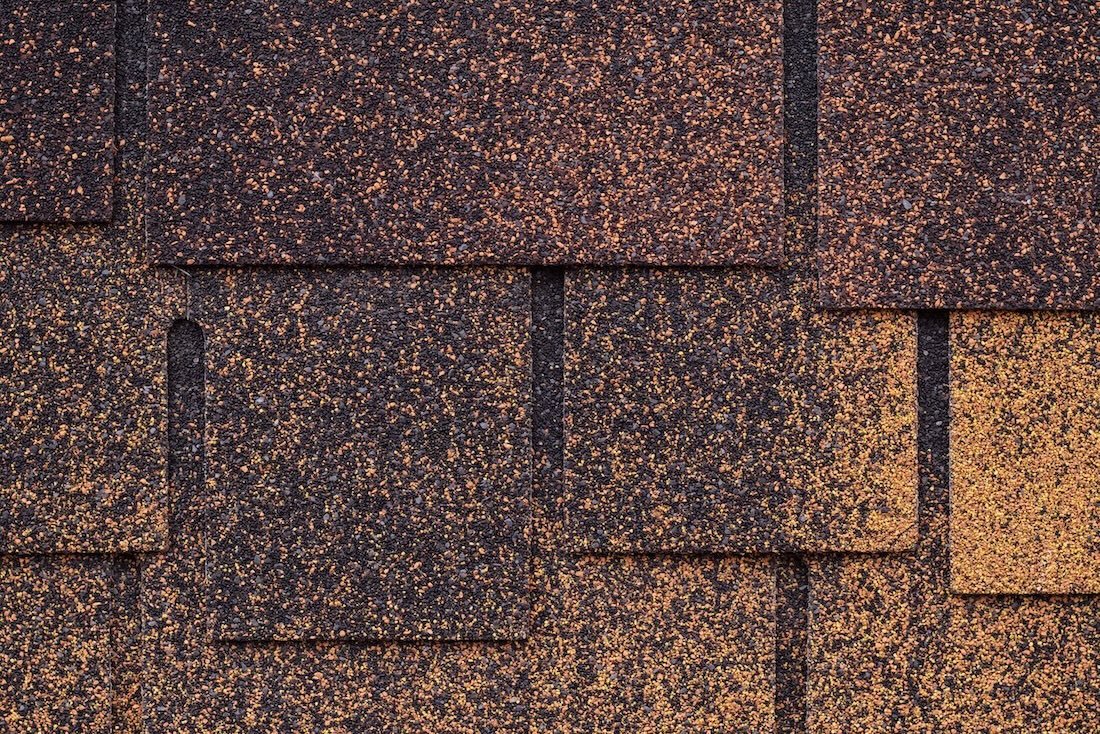 Close-up of asphalt shingles with a multicolored speckled appearance in shades of brown, black, and tan.