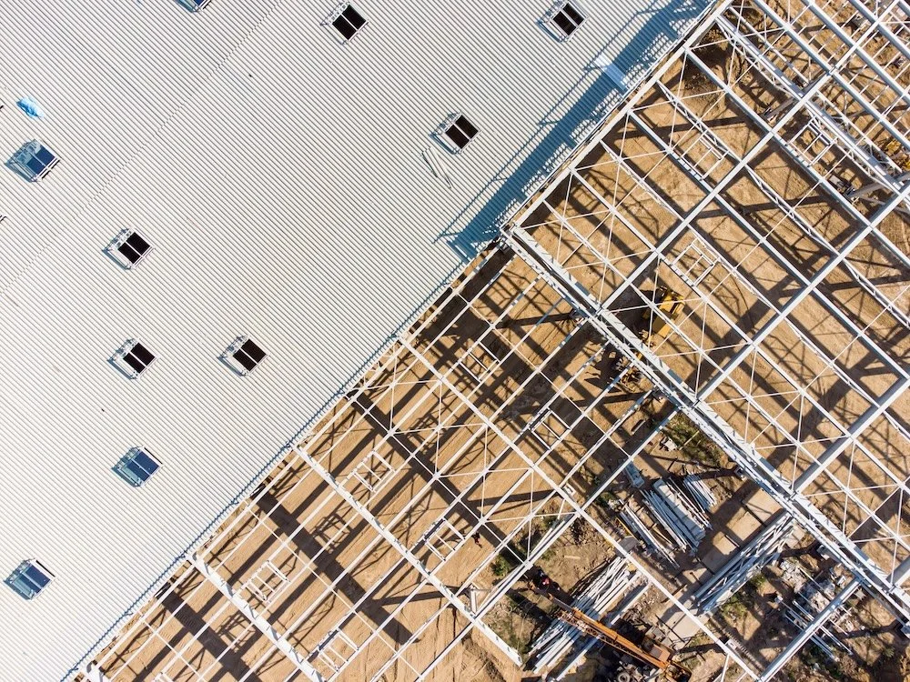 Aerial view of a building under construction with a metal framework and a partially completed roof.