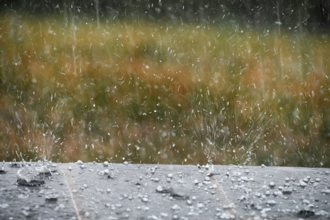 Close-up of a flat surface hitting hailstones, causing them to scatter and splash, with a blurred background.