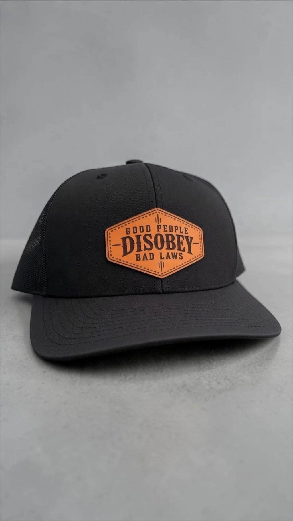 Black Richardson 112 trucker hat with genuine brown leather Good People Disobey Bad Laws patch.
