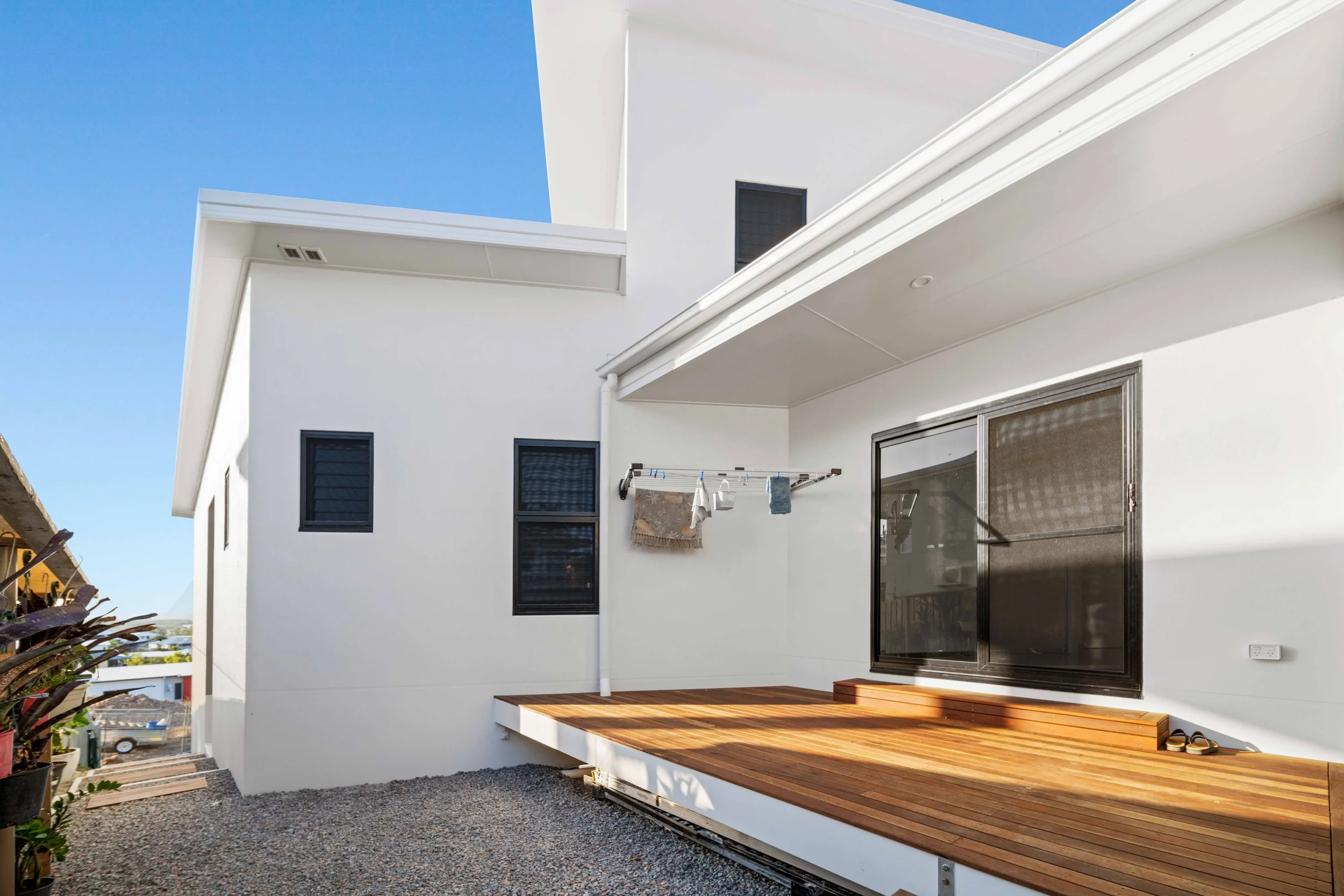 Modern white house with a small wooden deck and black-framed windows, laundry drying on a clothesline outside, under a clear blue sky.