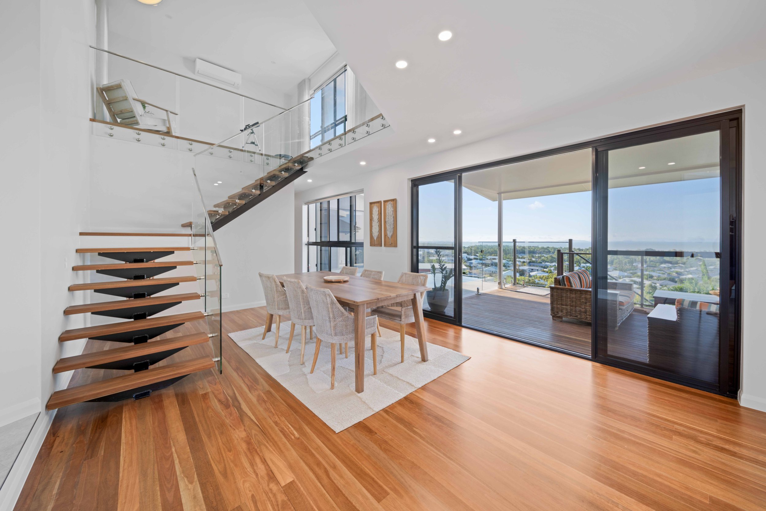 Open living/dining area with wooden flooring, a dining table with six chairs, and a glass sliding door leading to a balcony with outdoor seating and city view.