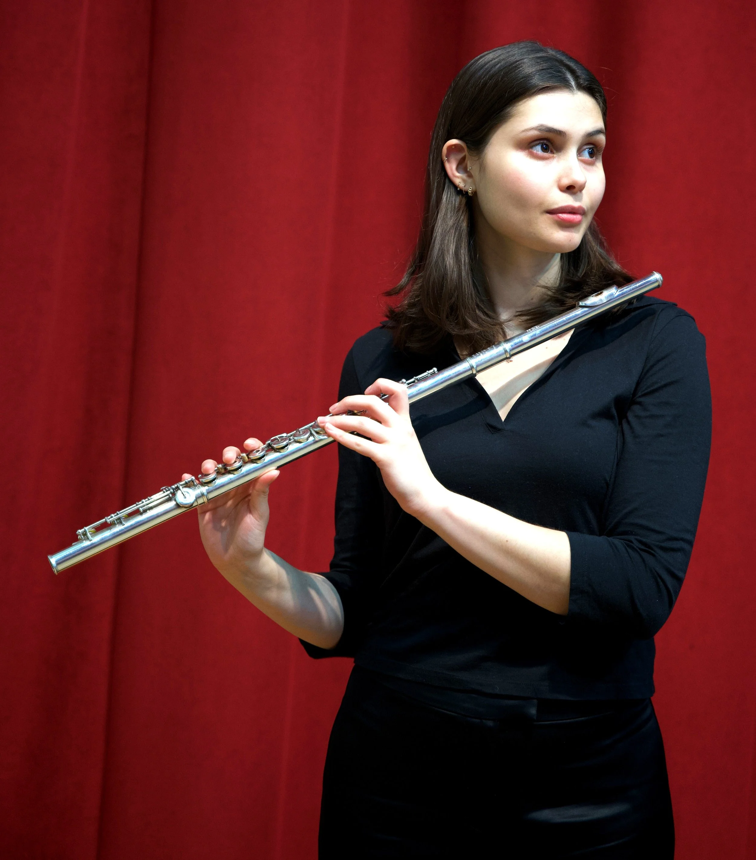Zoe Rabinowitz holding a silver flute against a red background.