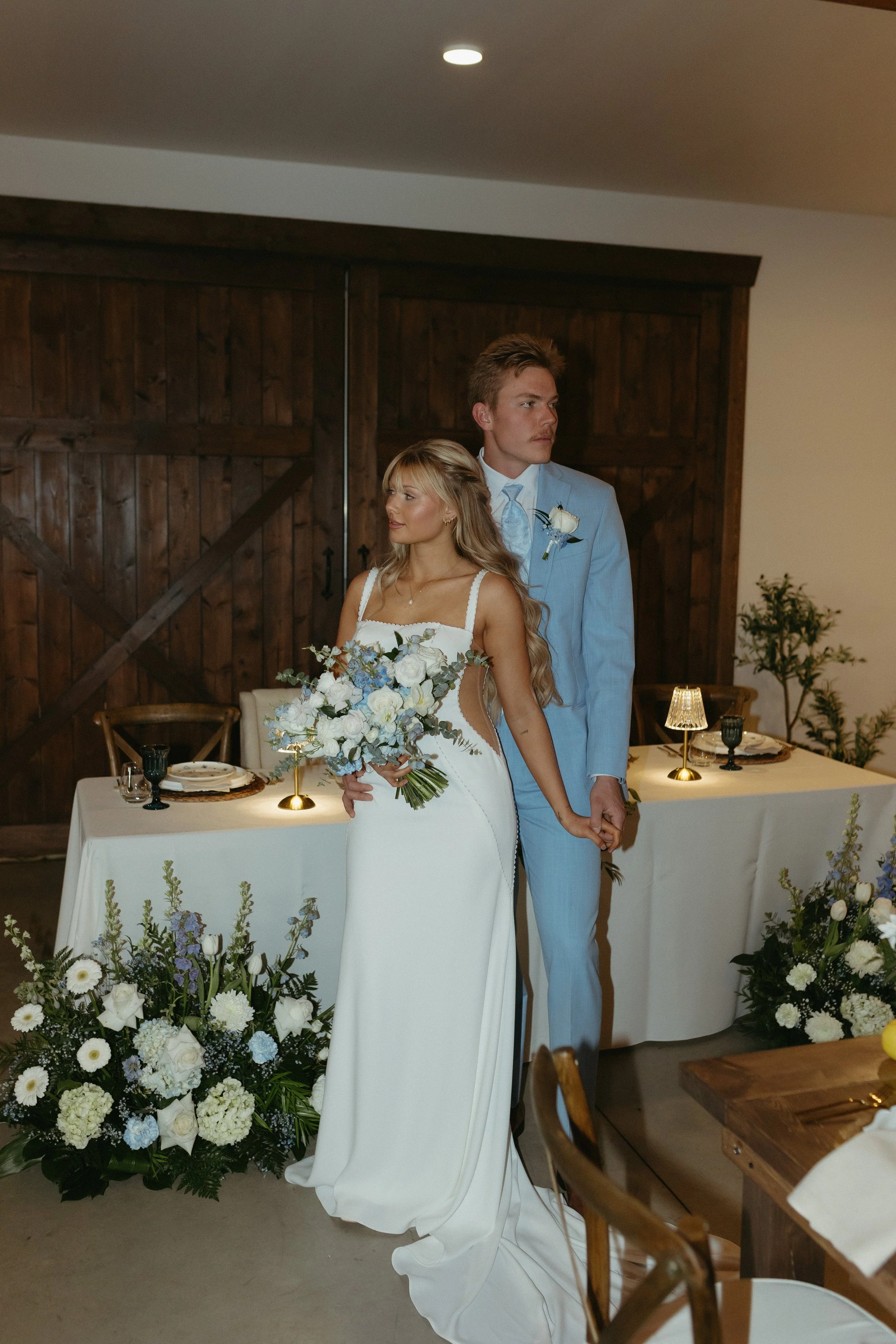 Bride and groom standing together at their wedding reception, surrounded by floral arrangements and decorated table settings.