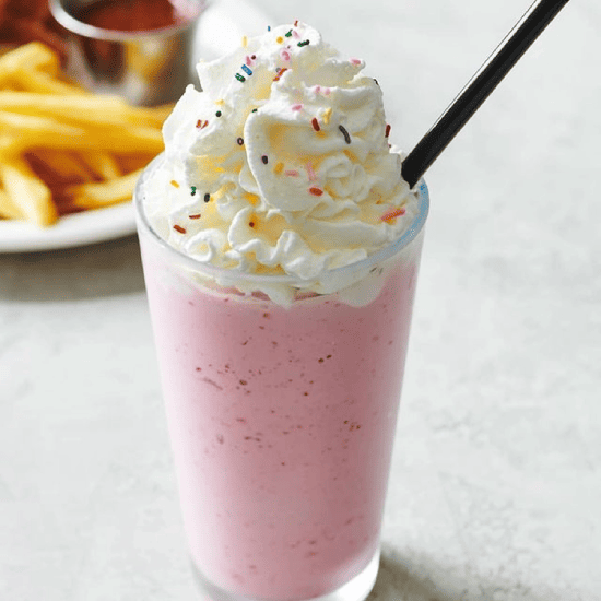 Pink milkshake topped with whipped cream and colorful sprinkles, with a black straw.