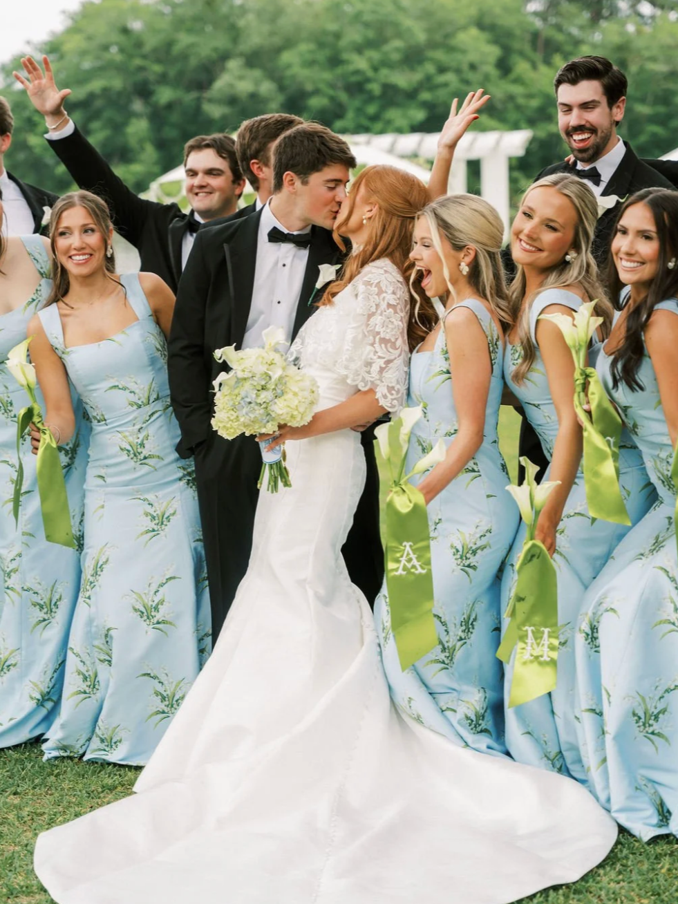 Bride and groom kissing surrounded by bridesmaids and groomsmen during a wedding celebration outdoors.