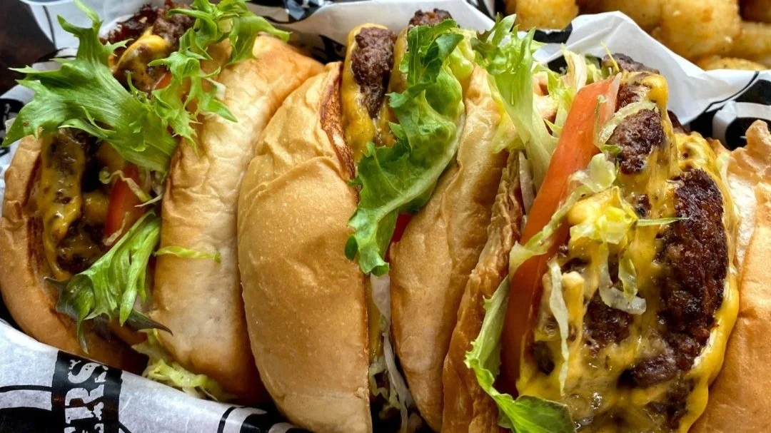 Three cheeseburgers with lettuce and tomato on a tray.