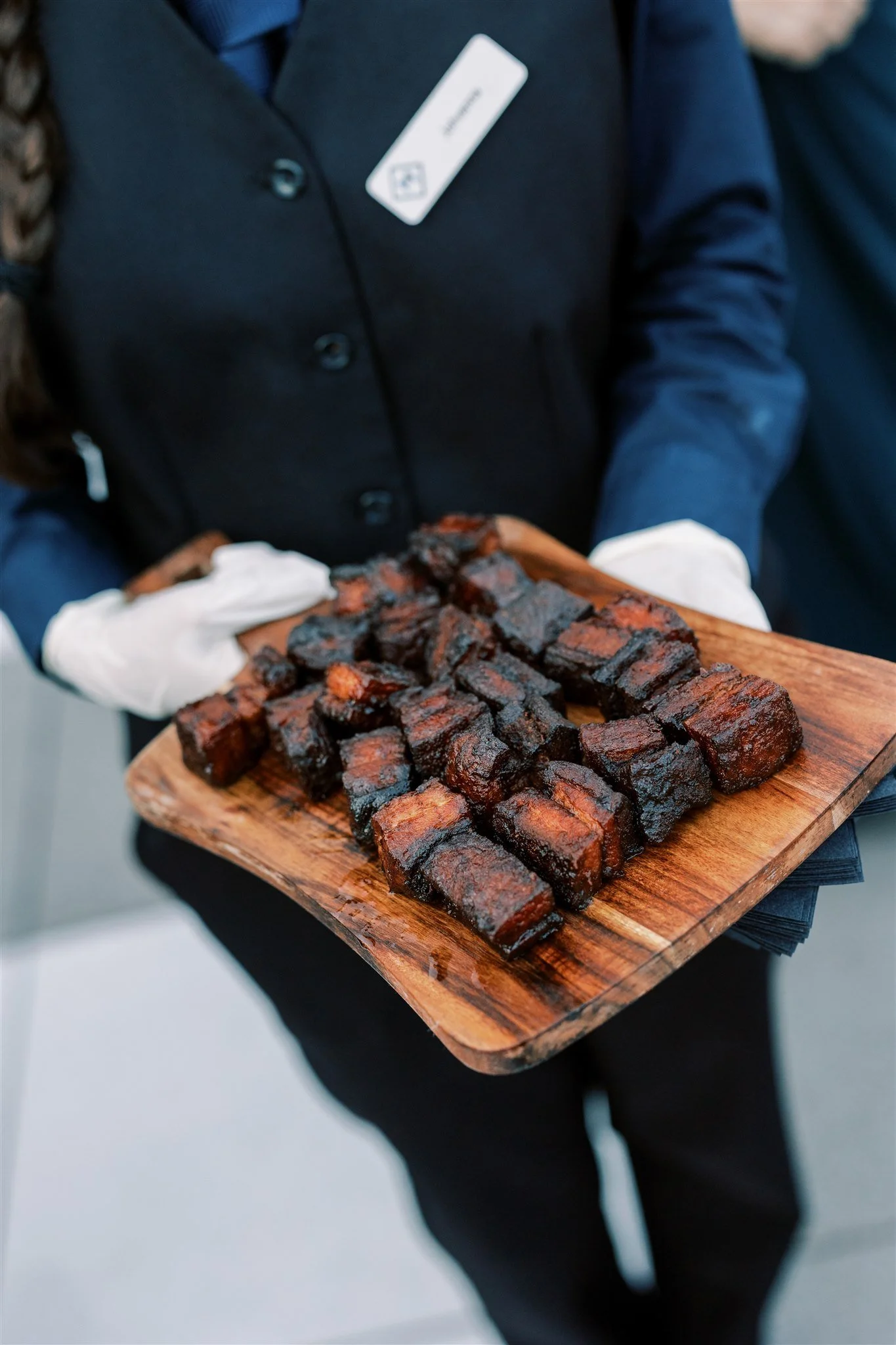 Catering server holding a wooden tray with smoked barbecue ribs.