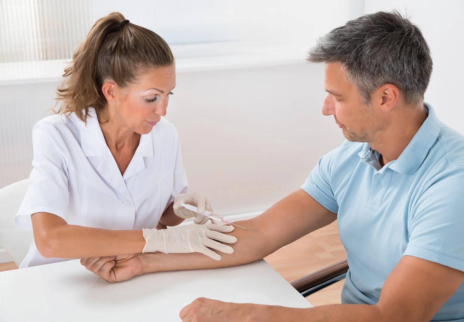 A healthcare professional, a woman, is drawing blood from a male patient using a syringe in a medical setting.