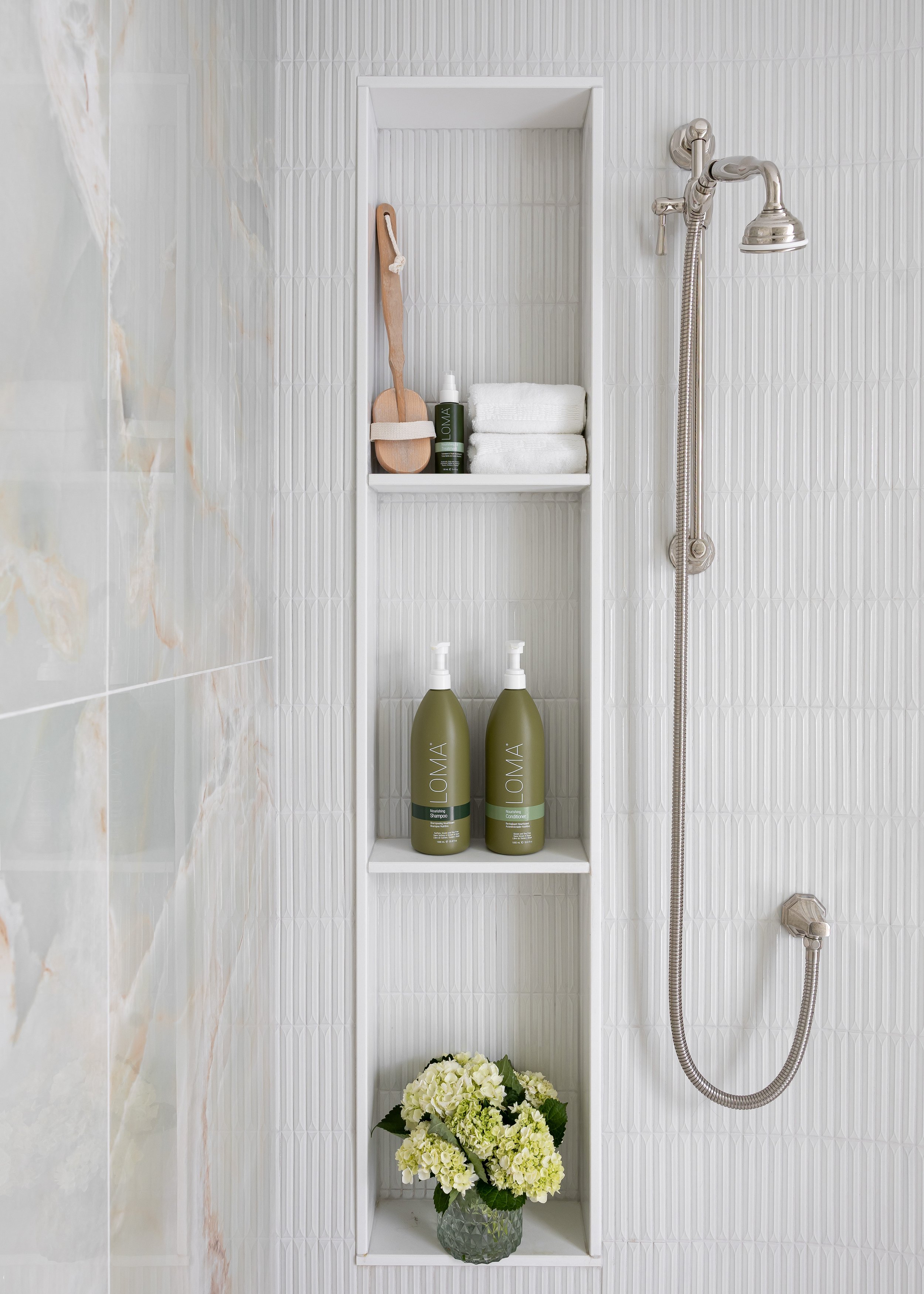 Custom-designed shower niche featuring integrated shelving and textured white tile for a spa-inspired bathroom renovation. Studio 7 Designs blends luxury finishes with functional storage to elevate everyday routines in this curated bath space.