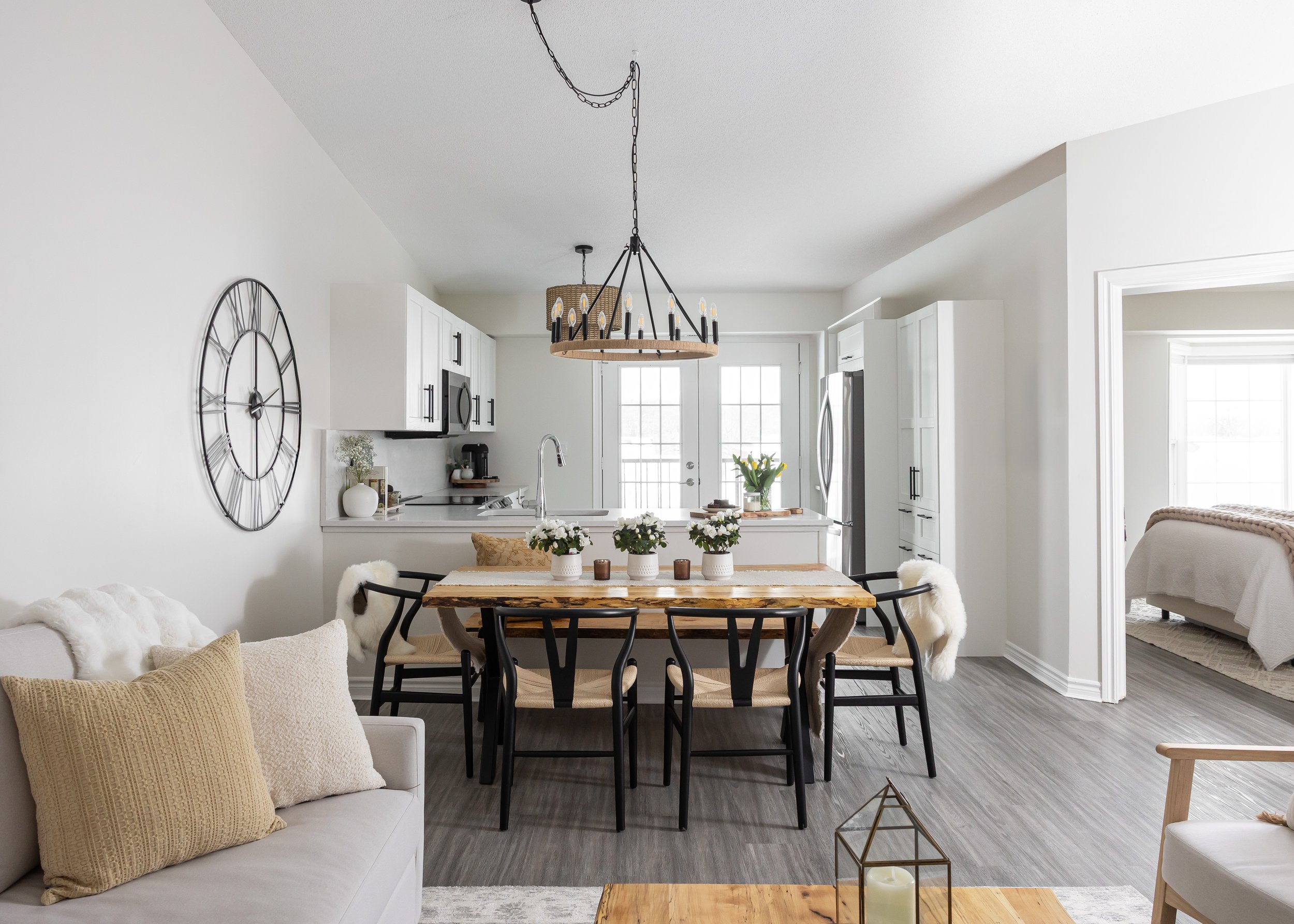 Modern farmhouse open-concept kitchen and dining area styled by Studio 7 Designs. Features a natural live-edge wood table with black chairs and a bench for space-saving seating. White shaker cabinets, matte black fixtures, and wood-and-iron chandelie