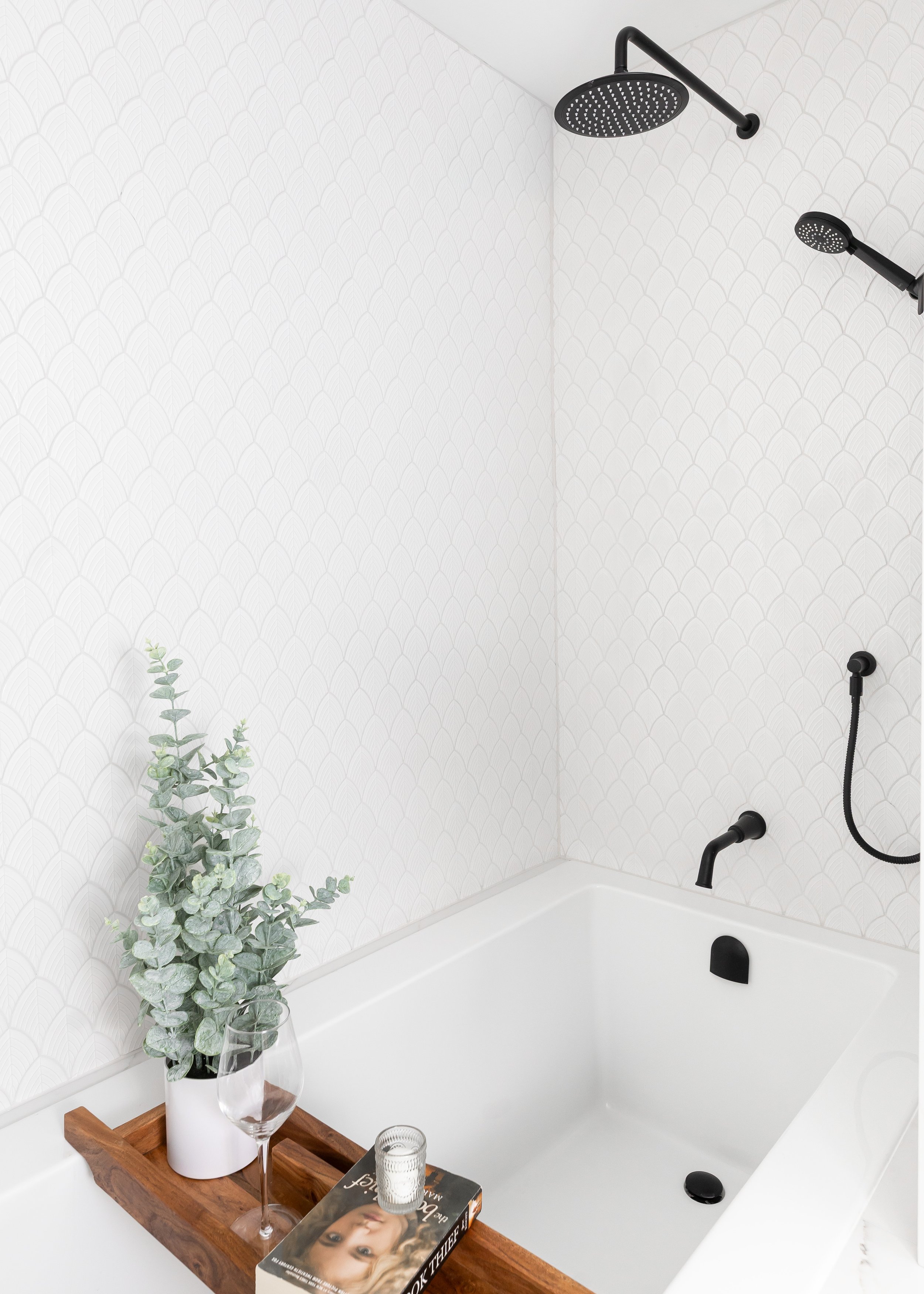 Modern minimalist bathtub design by Studio 7 Designs with black matte fixtures, scallop tile feature wall, and wood bath tray styling—luxury bathroom remodel idea.