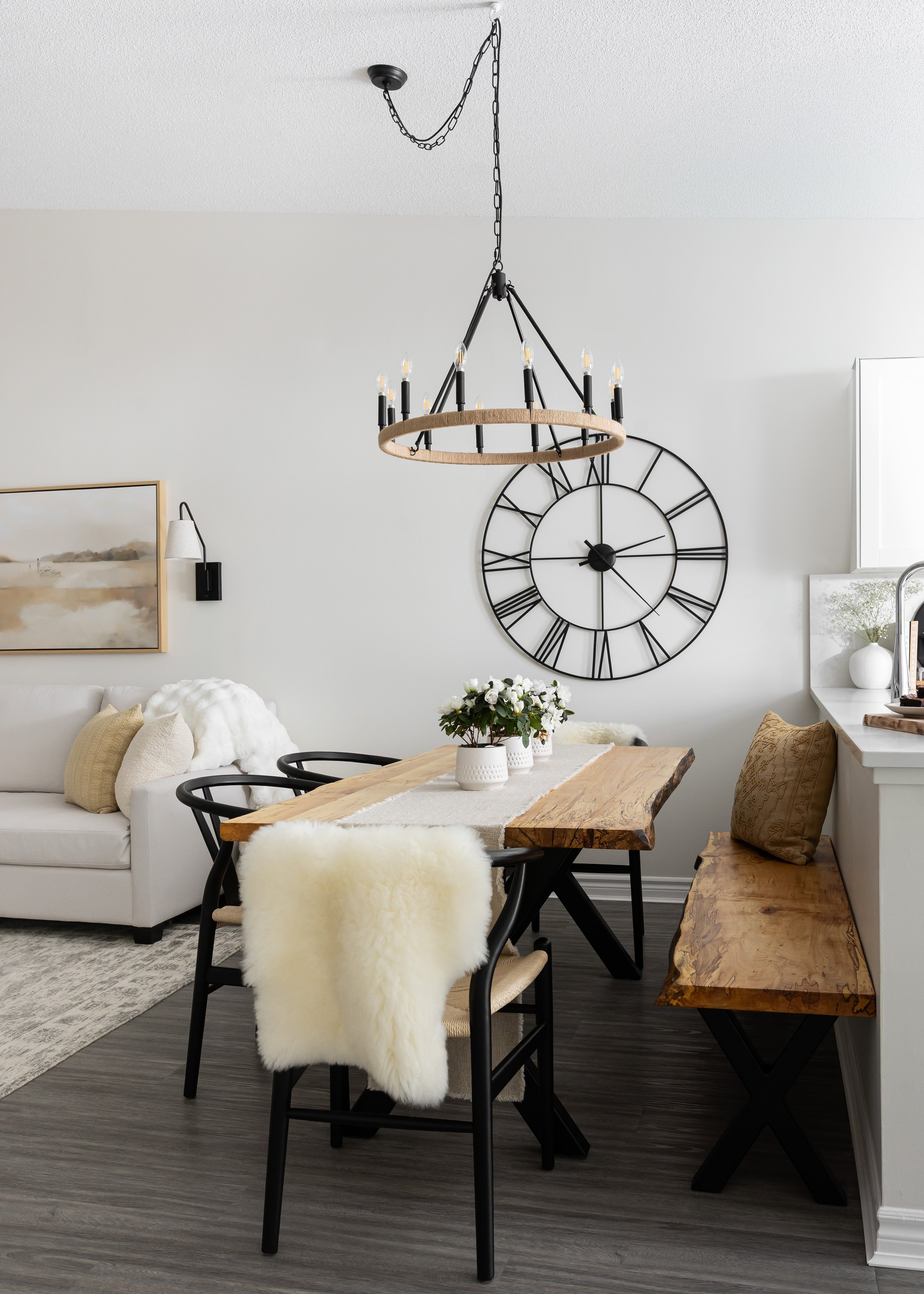 Modern rustic dining room styled by Studio 7 Designs, featuring a live-edge wood table, space-saving bench seat, black wishbone chairs, and cozy sheepskin throw—perfect for maximizing space in small homes or condos.