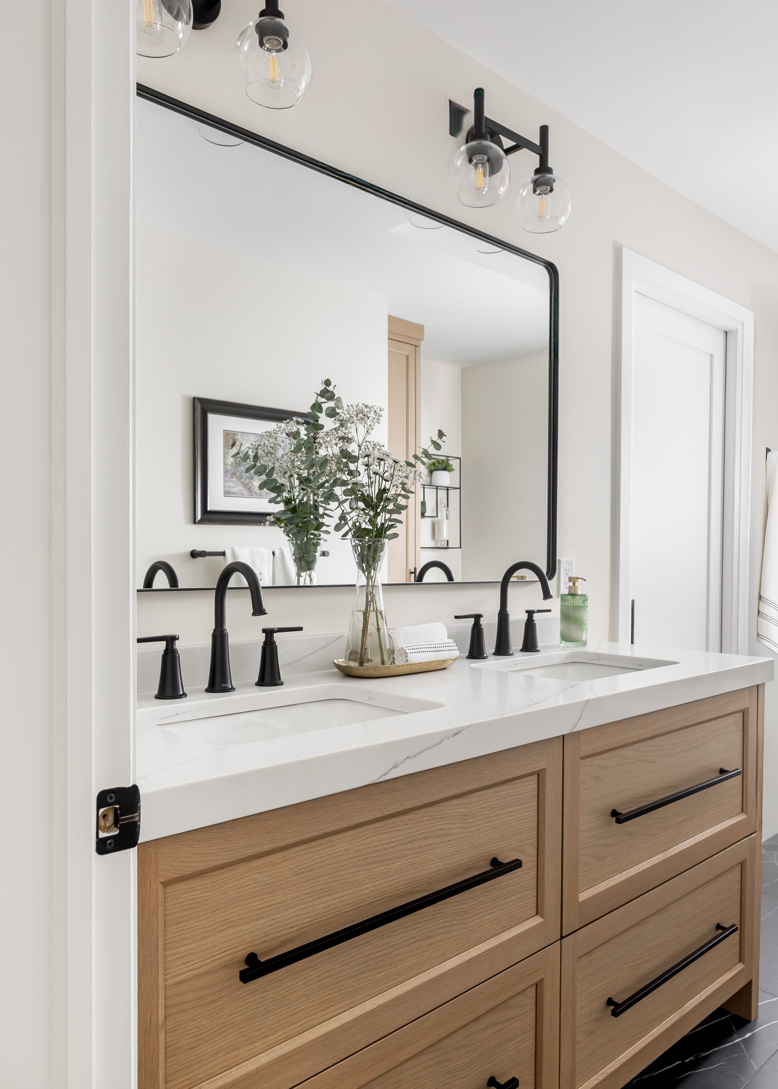 Custom double vanity bathroom design by Studio 7 Designs featuring natural wood cabinetry, white quartz countertop, matte black fixtures, and a large modern mirror—elegant bathroom renovation inspiration. Featuring thick counter.