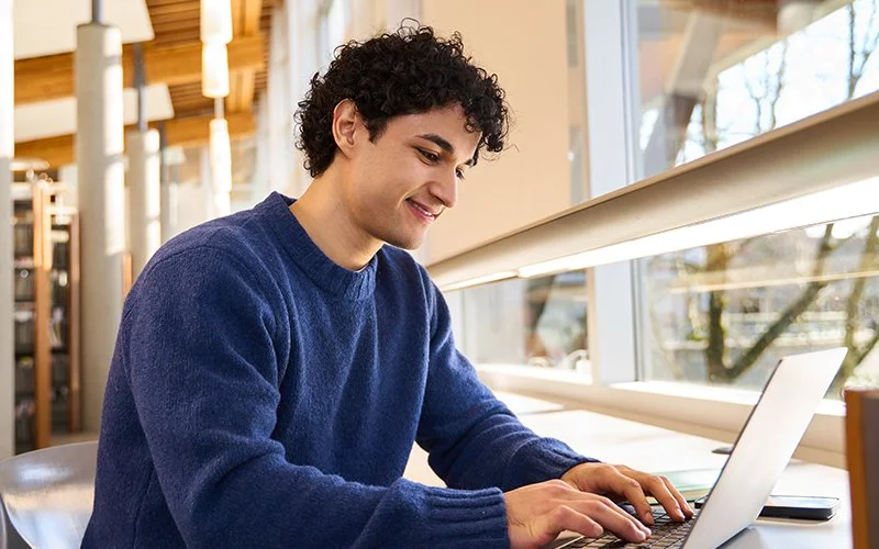 College student sitting in the library focused on his laptop