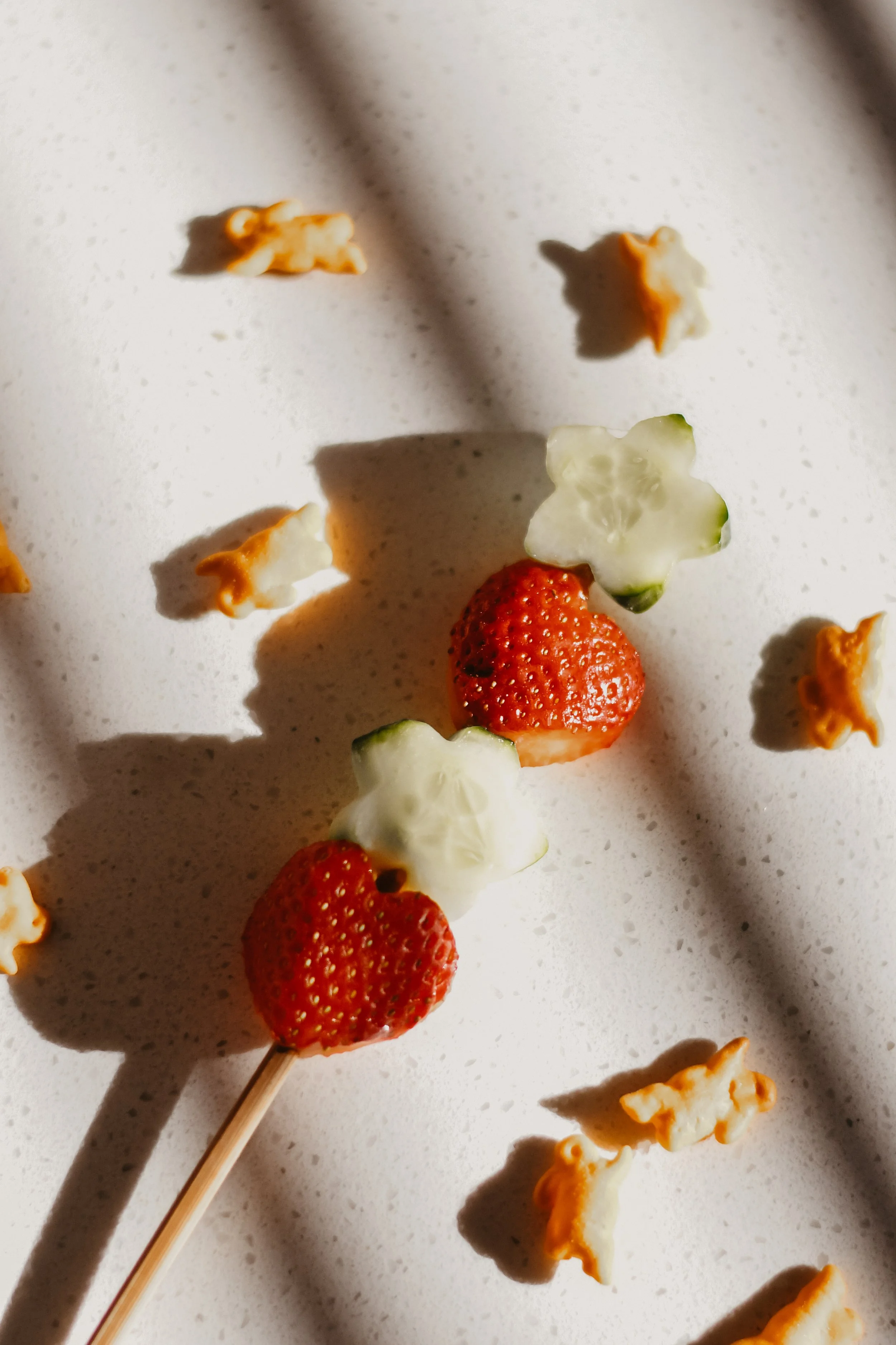 Close-up of strawberries and animal-shaped crackers on a white surface with shadows.