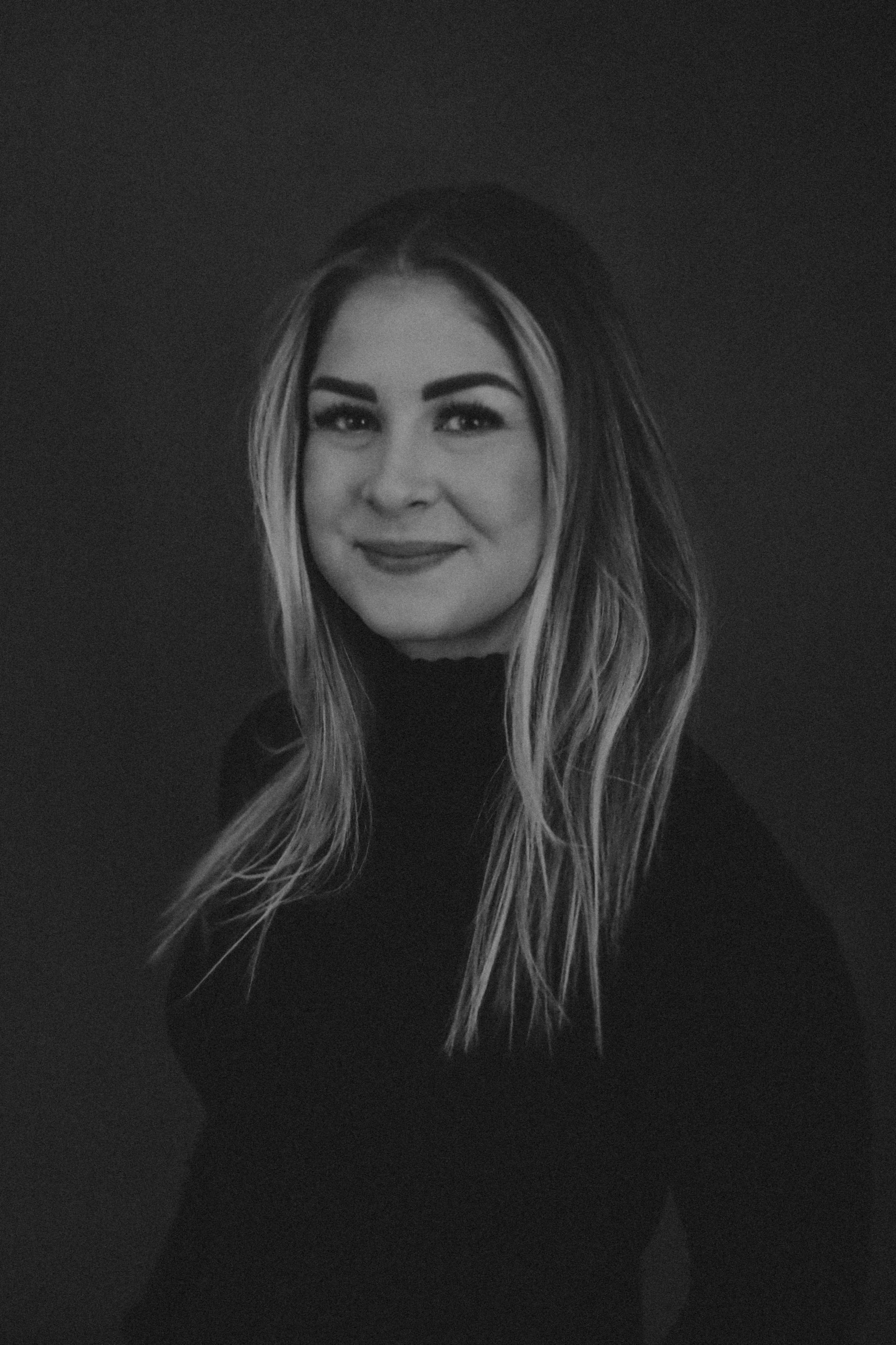 Black and white portrait of a smiling Pediatric Dietitian with long, wavy hair, wearing a dark turtleneck, against a plain background.